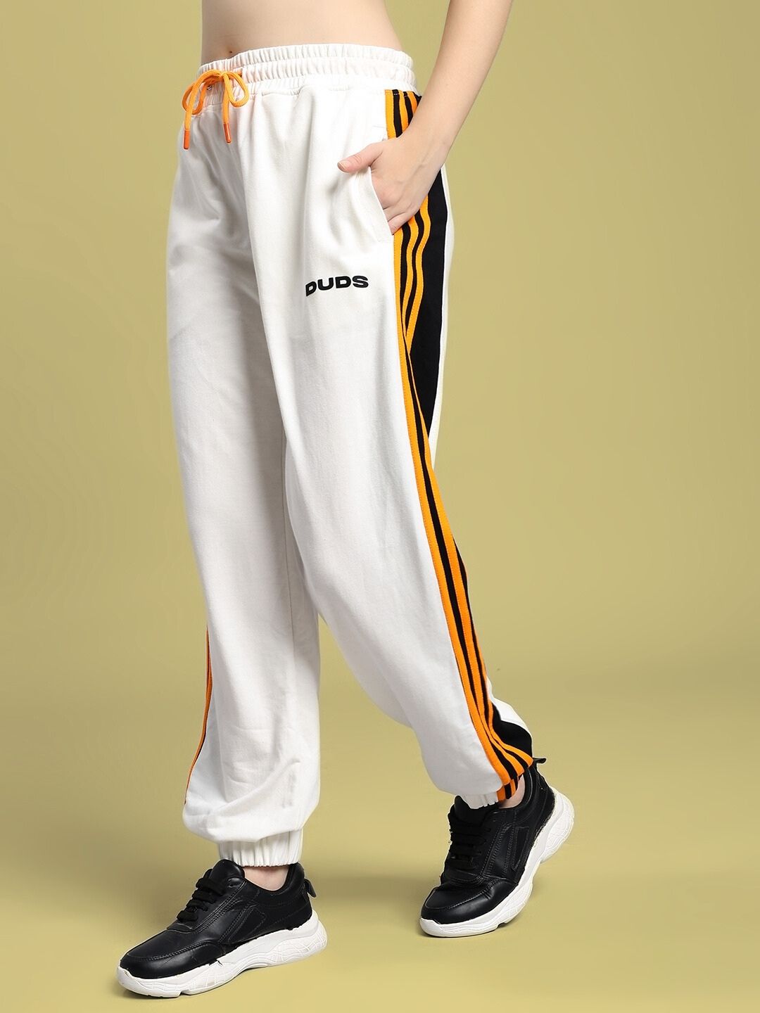 Woman wearing WOMEN'S COMFORT FLEX STRIPE JOGGER OFF-WHITE with black sneakers, off-white joggers featuring orange and black stripes.