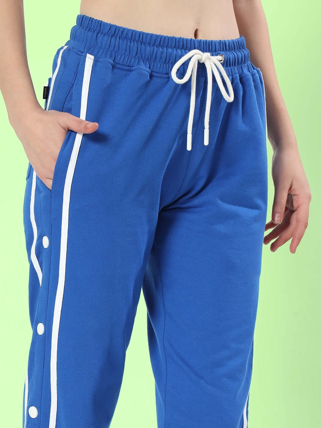 Women's contrast panel joggers in blue with white drawstring, featuring side pockets and button accents, shown against a green background.