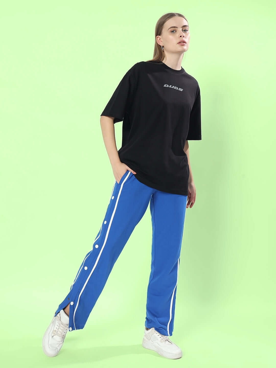 Woman wearing blue contrast panel joggers paired with a black DUDS t-shirt, standing against a light green background.