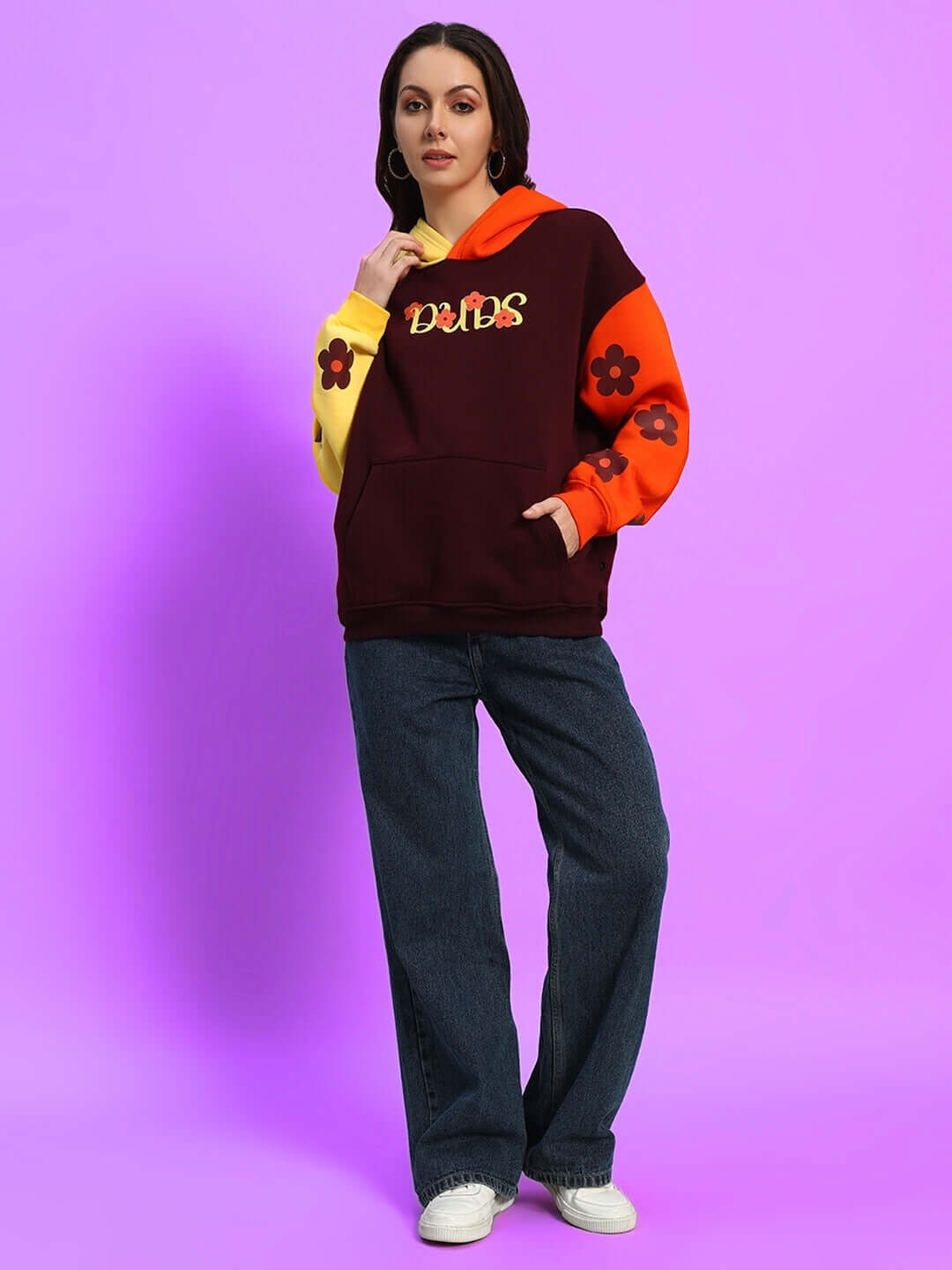 Woman wearing oversized fleece hoodie with multi-color design and cosmic graphics, paired with jeans, on a purple background