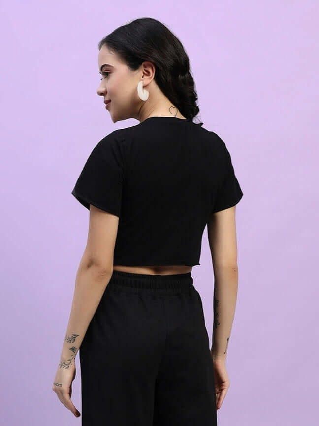 Woman wearing black cotton crop-top, side view, against purple background, showcasing stylish and comfortable fit with short sleeves.