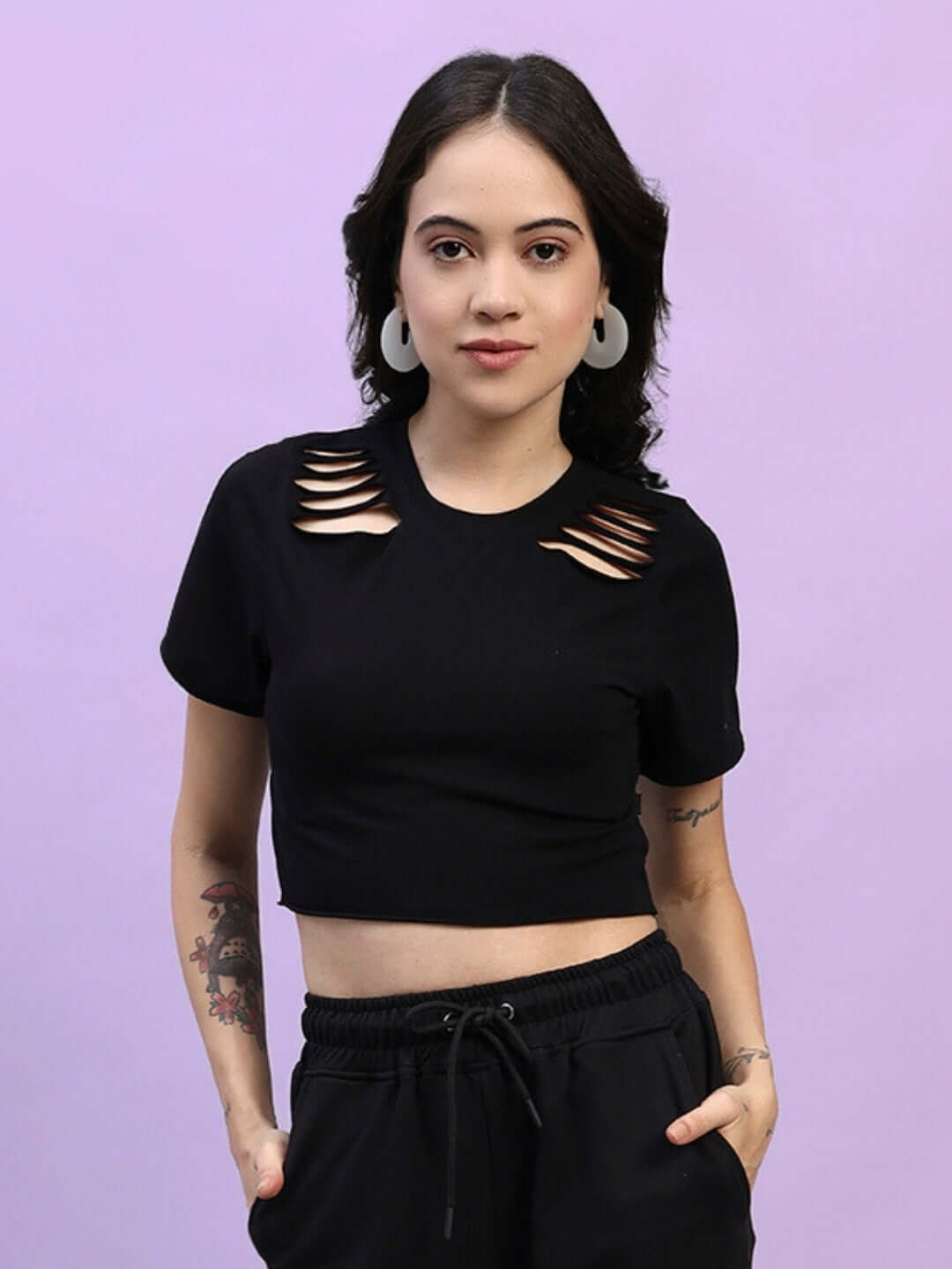 Woman wearing a black cozy crop-top made from 100% cotton Lycra fabric, showcasing cut-out shoulder design, standing against a purple background.