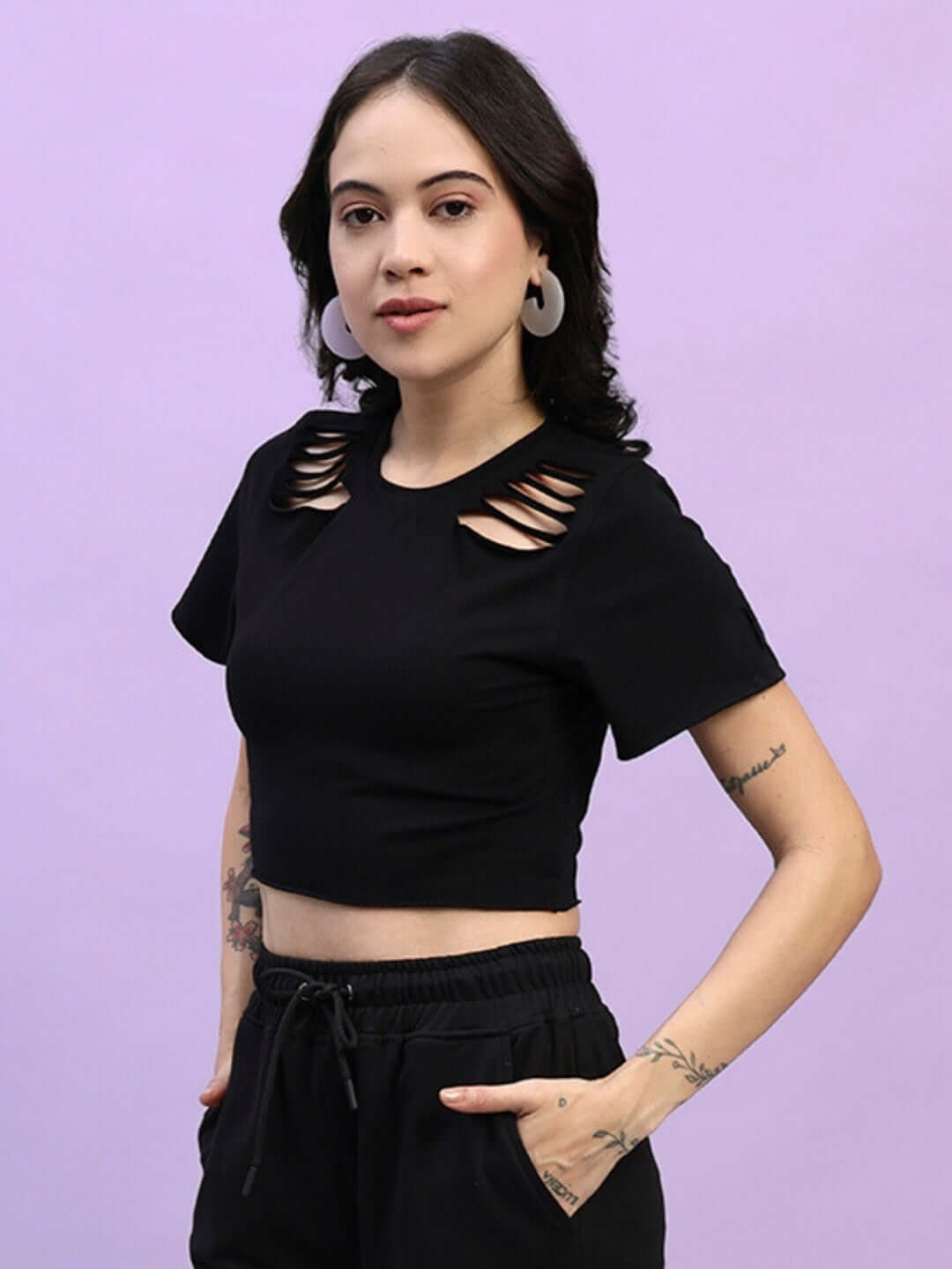 Woman wearing a black women's cozy crop-top crafted from premium cotton fabric, featuring stylish cutouts, standing against a purple background.