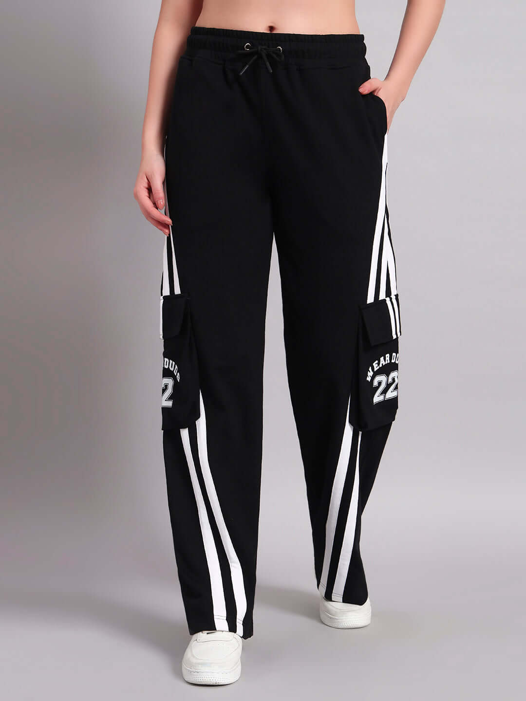 Women's black relaxed-fit joggers with multi pockets, featuring white side stripes and wearing white sneakers.
