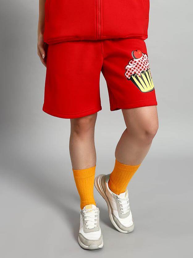 Woman wearing WOMEN CUPCAKE FLEECE SHORTS RED with cupcake design, paired with sneakers and orange socks for a bold streetwear look.