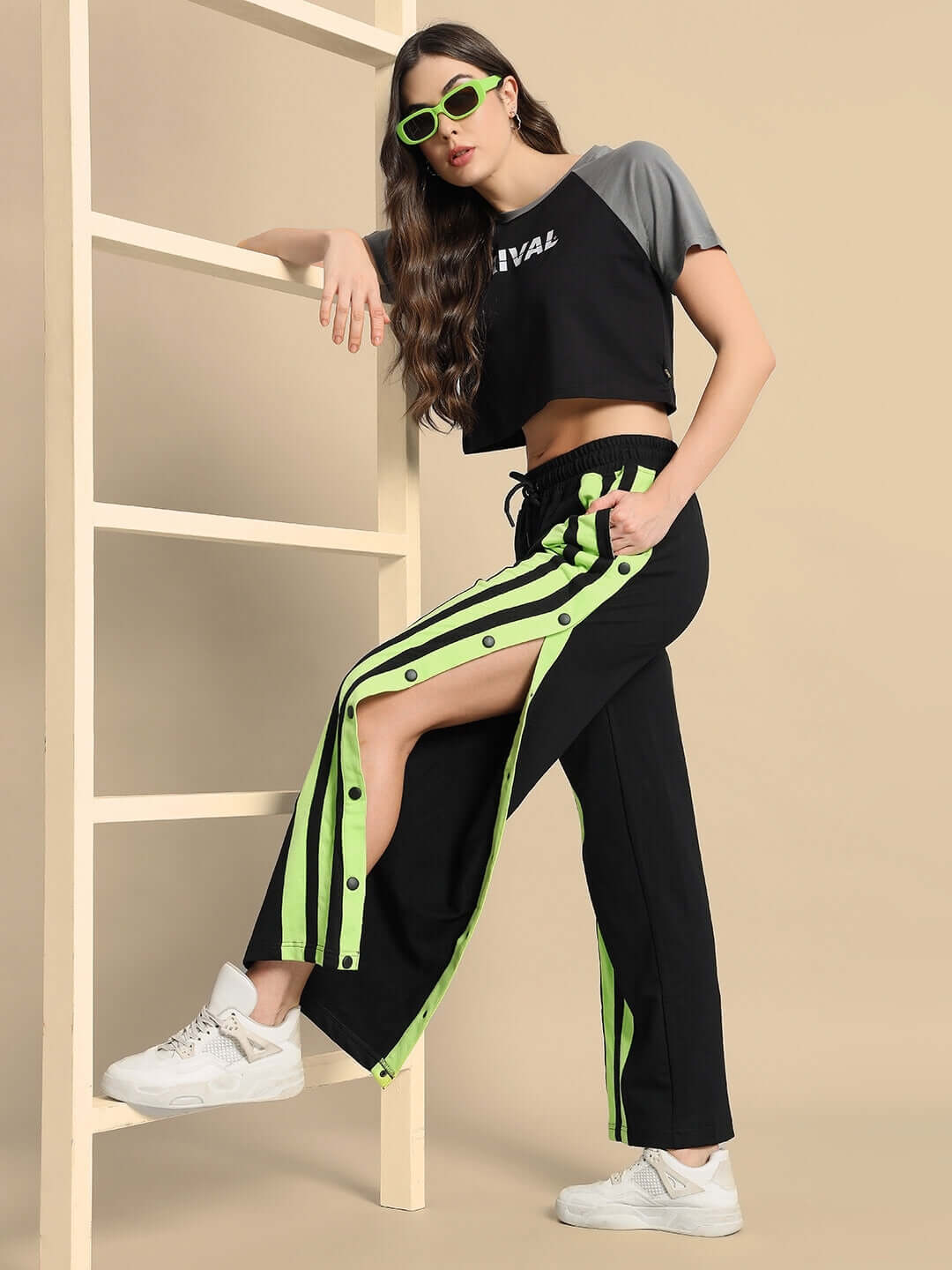 Woman modeling black joggers with neon green stripes, styled with a cropped top and sunglasses, highlighting trendy casual fashion.