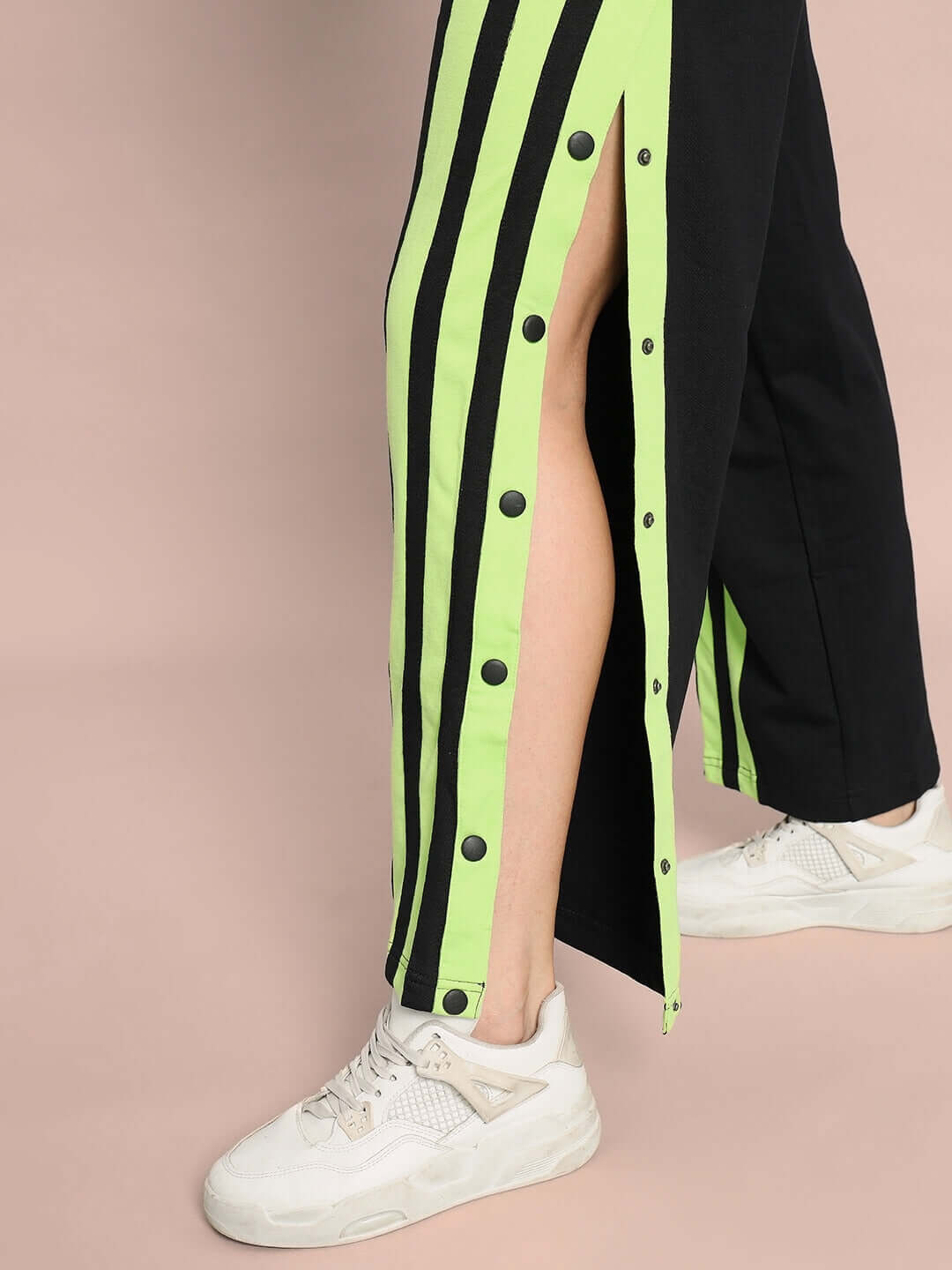 Close-up of black joggers with neon green stripes, featuring side snap buttons and worn with white sneakers.
