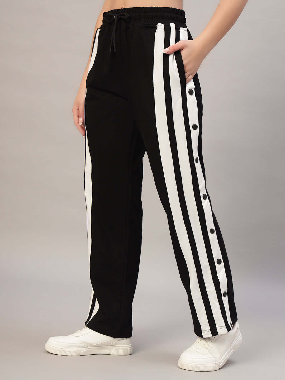 Women's black and white joggers with side stripe design and button details, worn with white sneakers.