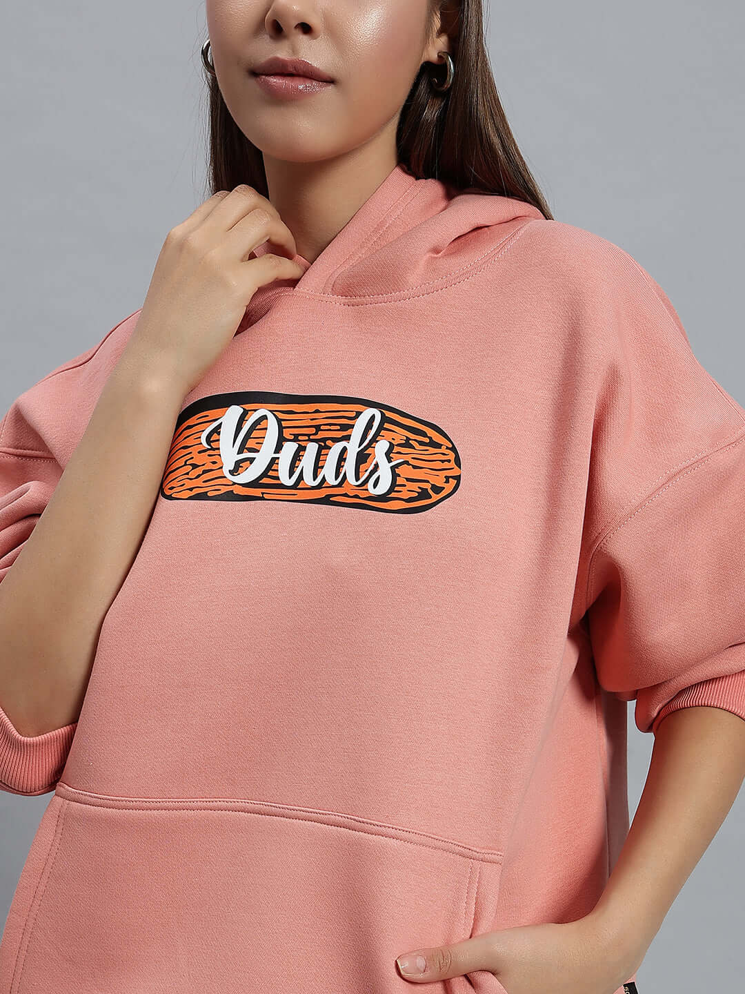 Woman wearing a peach Deliberate Fleece Hoodie with 'Duds' embroidered logo, showcasing a stylish and cozy look.