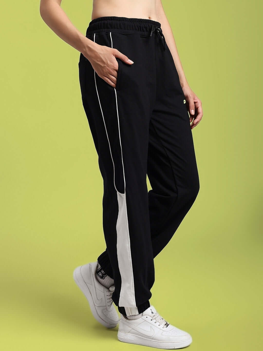 Model wearing black women's Denver relaxed fit joggers with white stripe, casual style, side view, on green background.