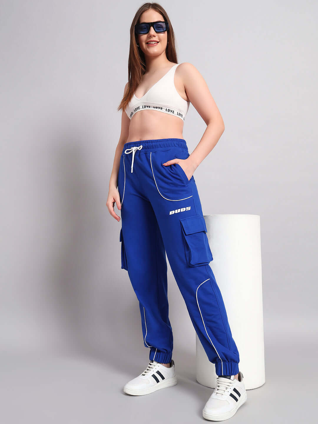 Model wearing women's blue Deveno relaxed-fit joggers with cargo pockets, paired with a crop top and sneakers.