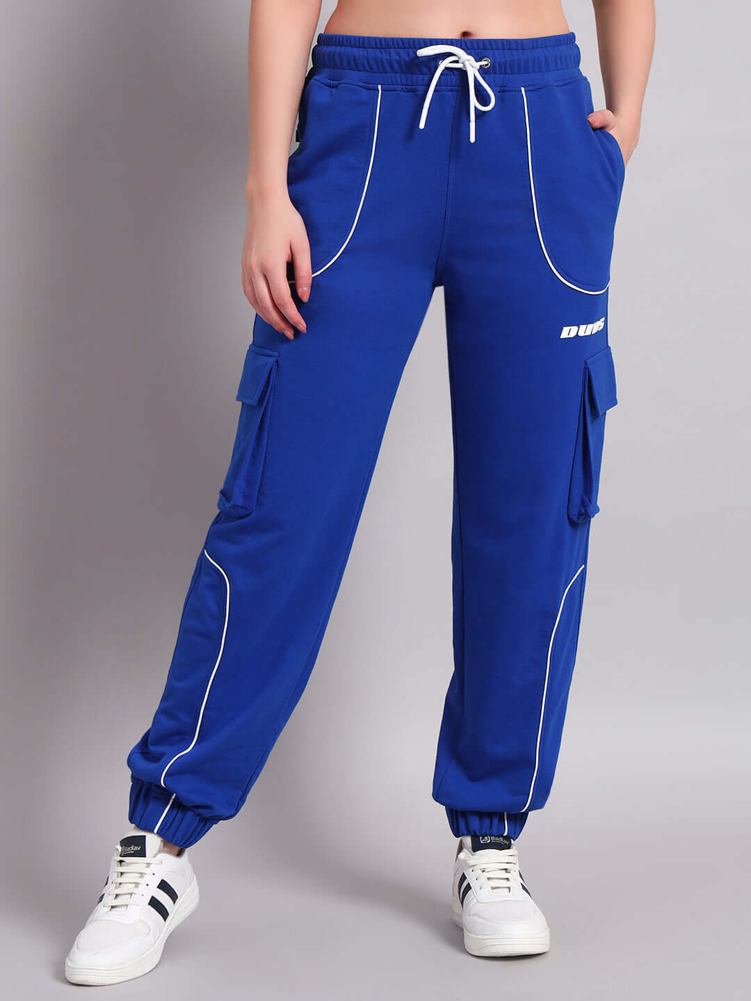 Model wearing blue women's relaxed-fit joggers with white piping design and sneakers, showcasing casual outfit style.