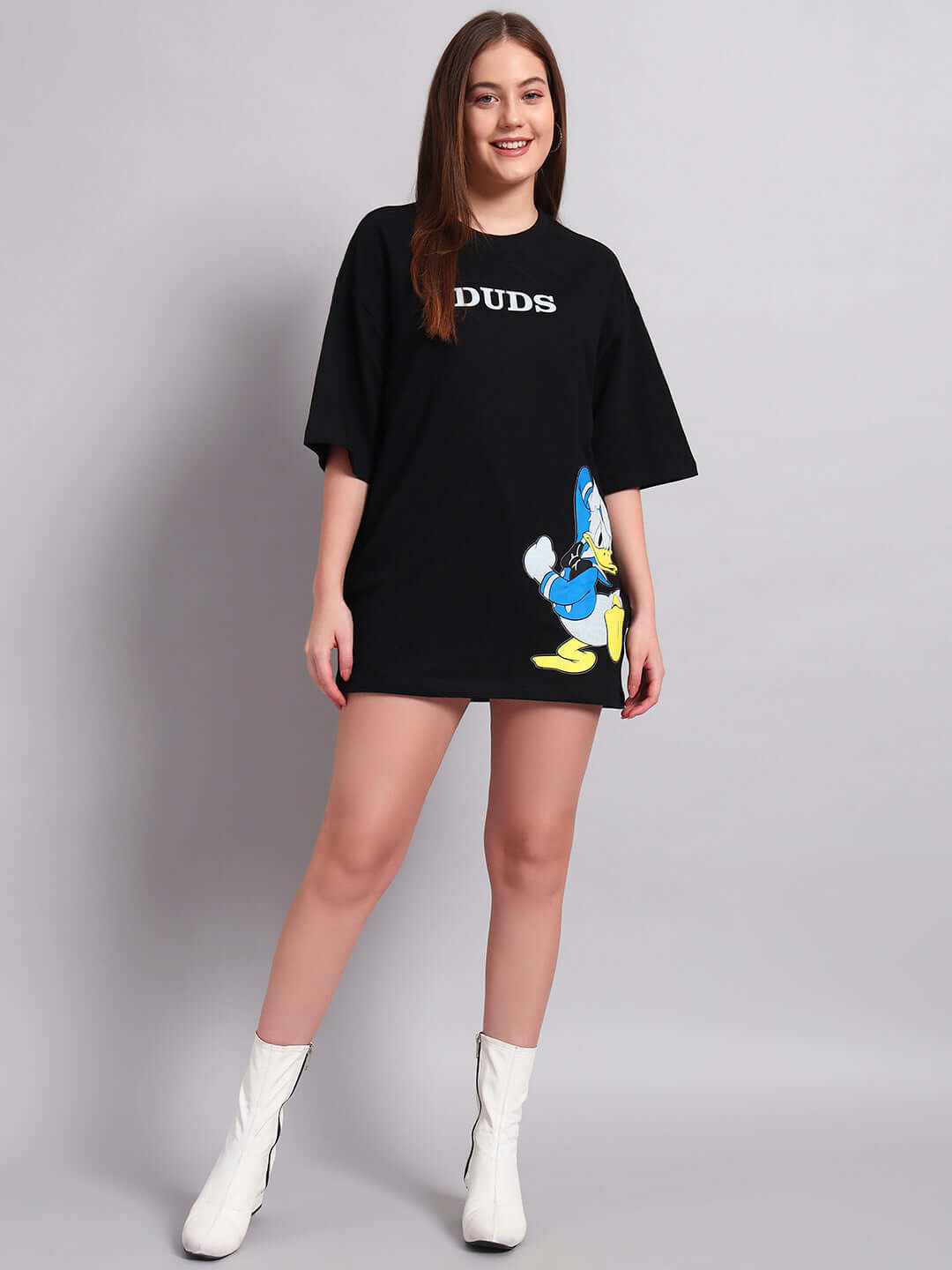 Woman wearing oversized black Donald Duck printed T-shirt, premium cotton blend, styled with white boots, showcasing casual fashion.