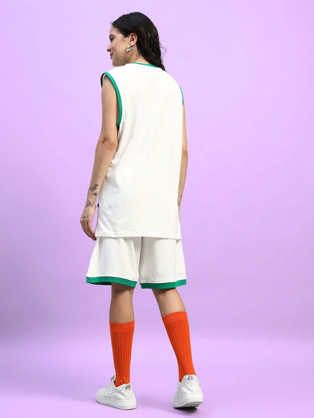 Back view of model wearing WOMEN'S DRIBBLE CO-ORD SET OFF WHITE with orange socks and white sneakers, purple background