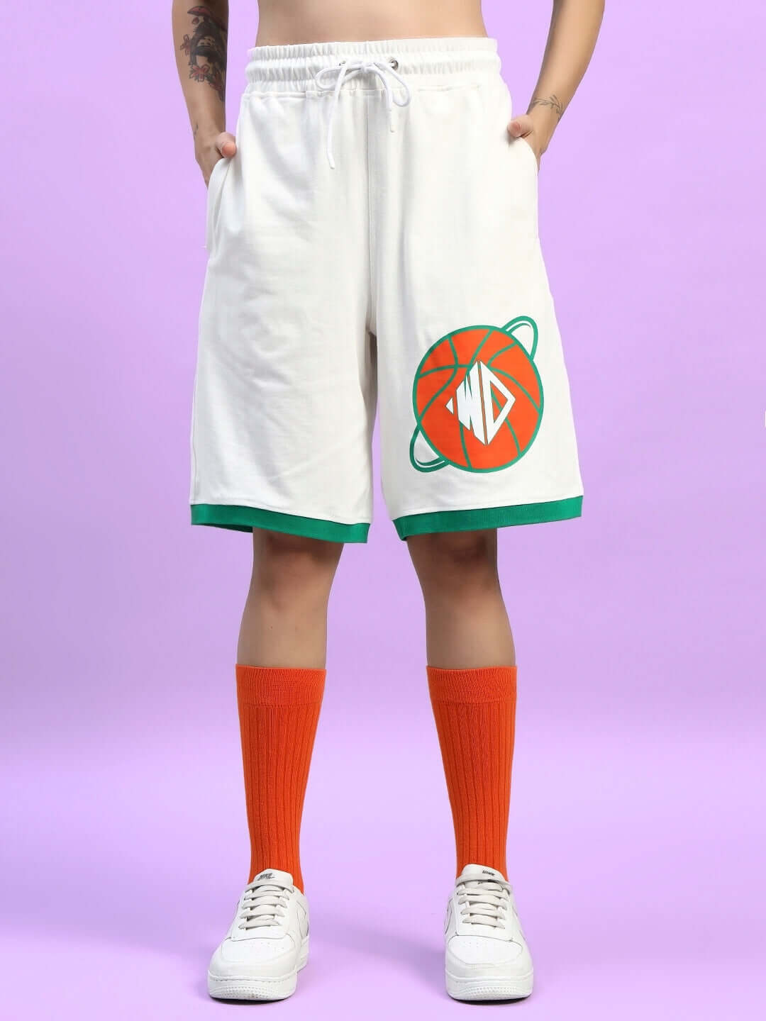 Woman wearing WOMEN'S DRIBBLE SUMMER SHORTS OFF-WHITE with orange socks and white sneakers, featuring a stylish graphic on a lilac background.