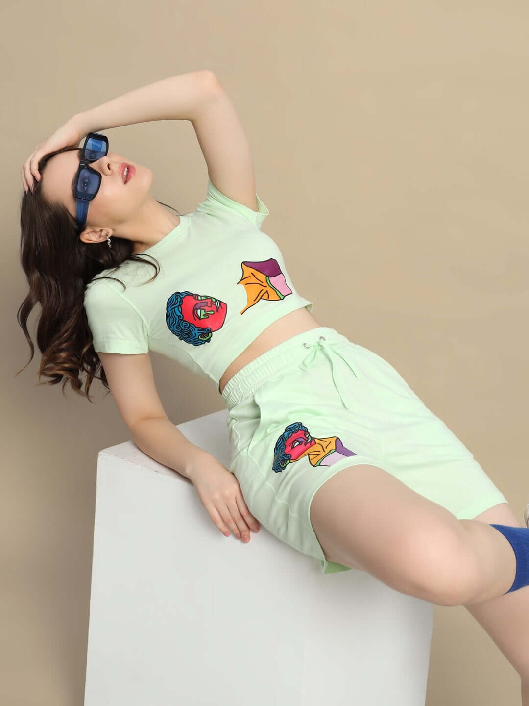 Woman wearing Women's Drip God Co-ord Set in Nyanza Green with colorful print, lying on a white block, showcasing stylish fashion.
