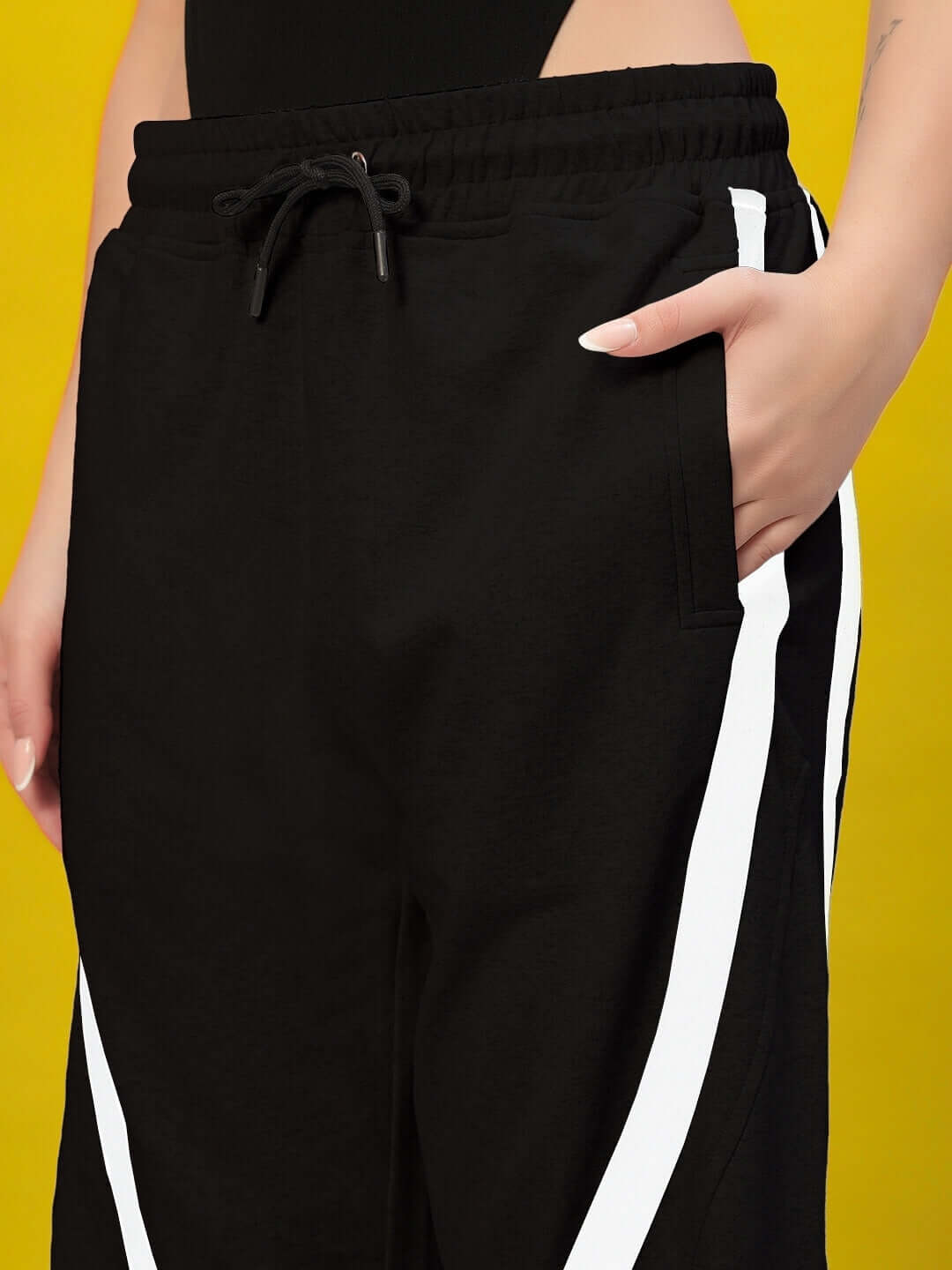Close-up of Women's DUDS Frame Joggers in black, featuring a side pocket and white stripes, against a yellow background.
