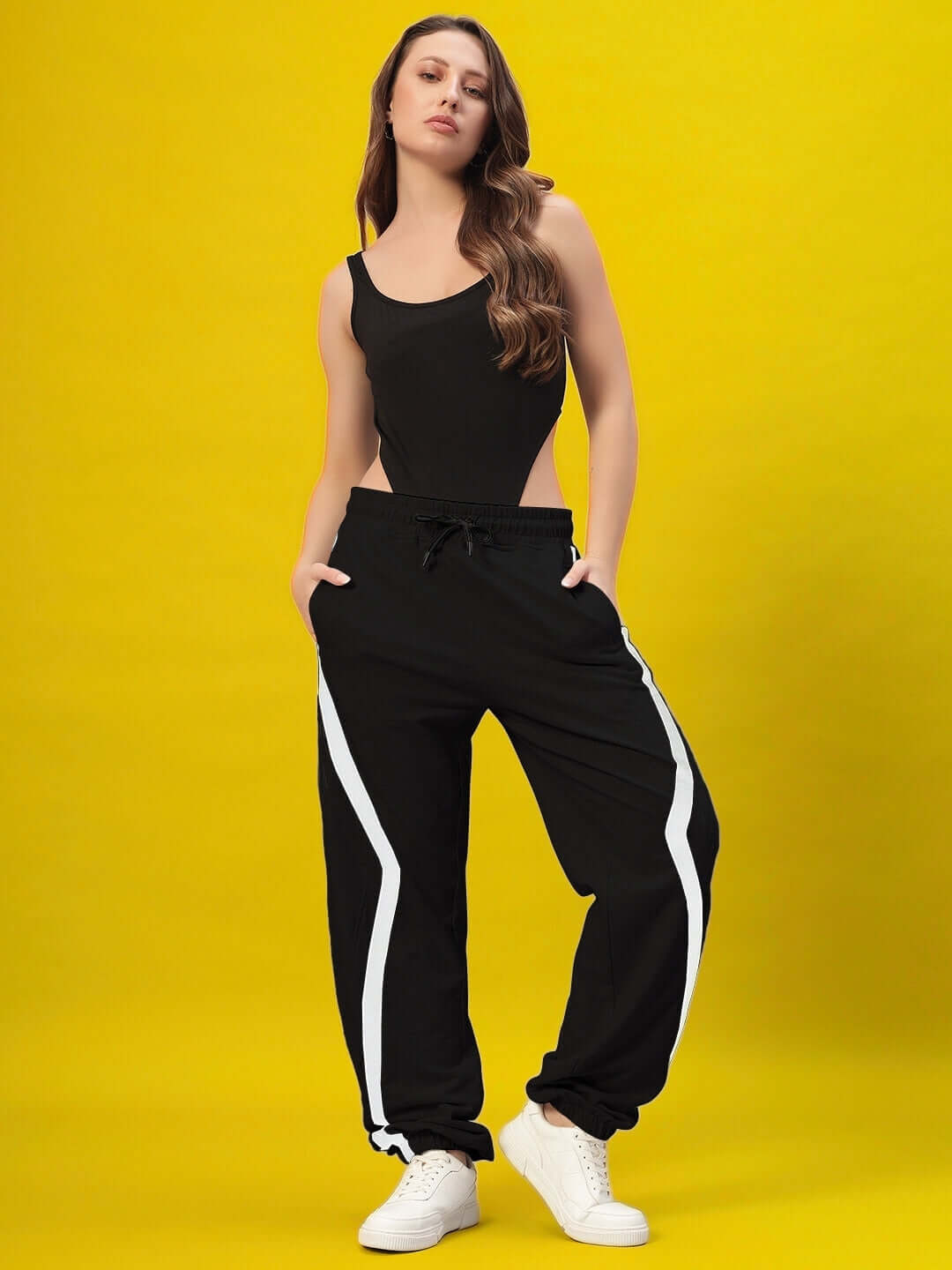 Model wearing Women's DUDS Frame Joggers in black with white stripes, showcasing custom fit options and comfort on a vibrant yellow background.