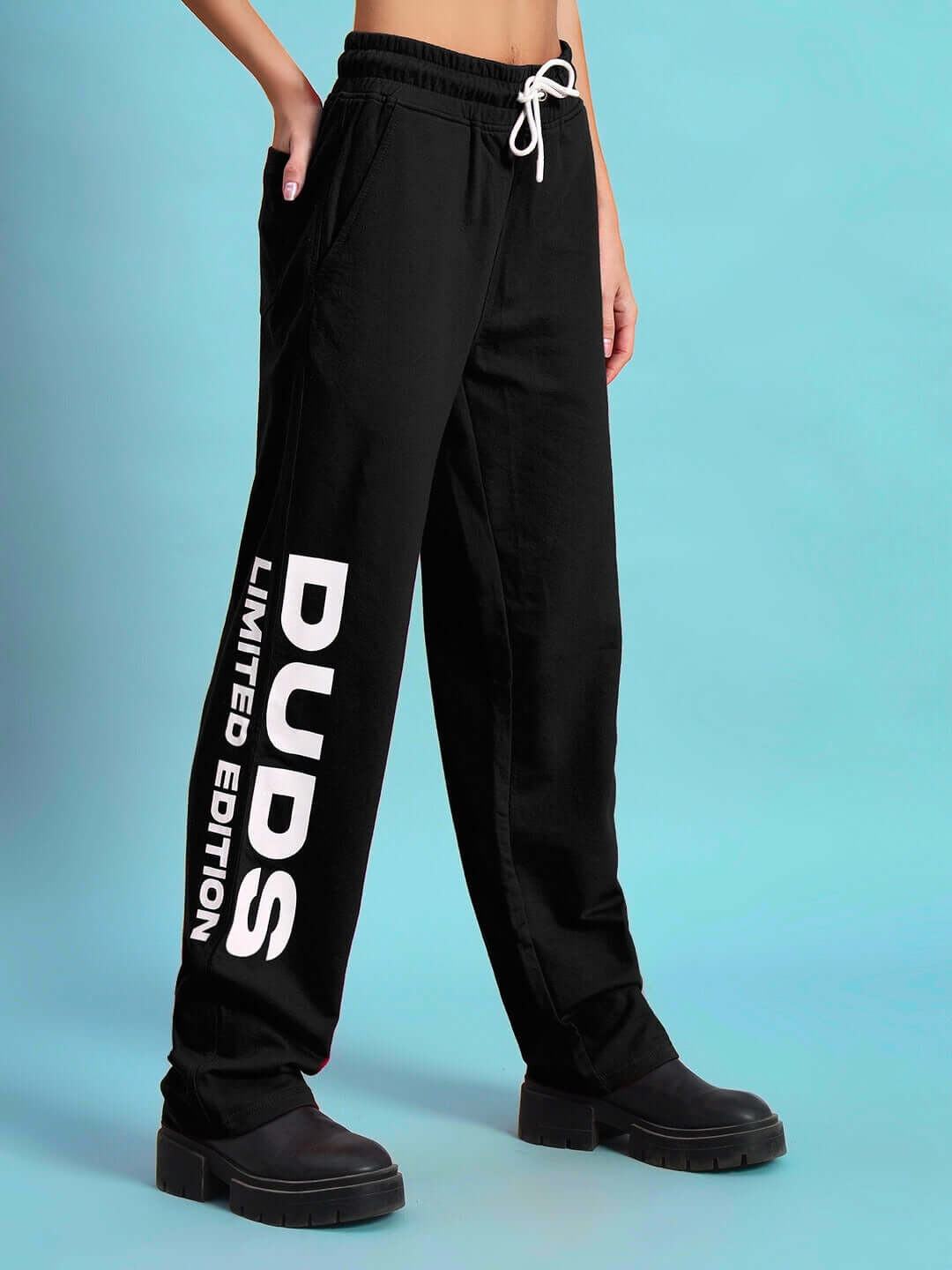 Black women's DUDS limited edition jogger pants with white drawstring and text, worn with black boots, highlighting casual style.