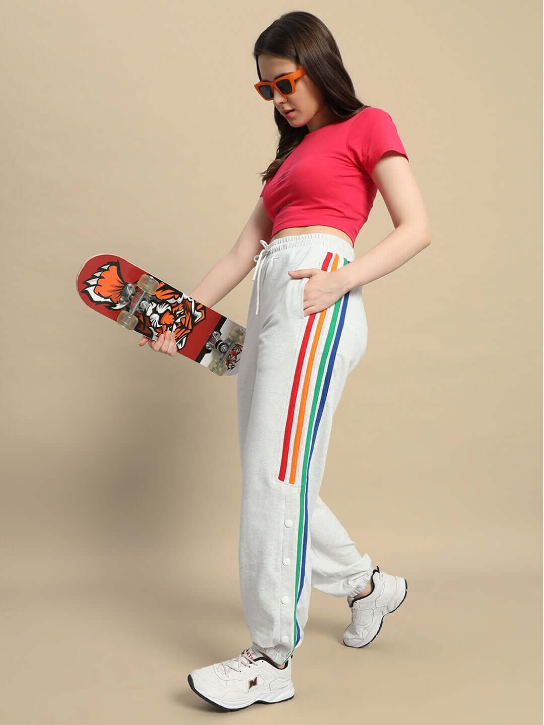Model wearing Women's DUDS Prism Colorful Stripe Joggers in Melange Grey, holding a skateboard, showcasing vibrant rainbow side stripes.