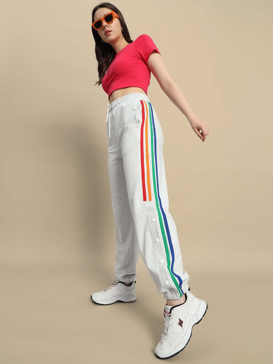 Woman wearing melange grey joggers with colorful stripes, paired with a red top and sunglasses, showcasing trendy DUDS fashion.