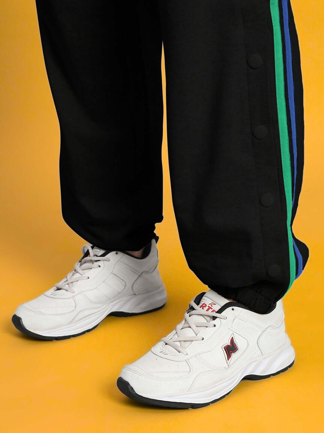 Close-up of Women's DUDS Prism Colorful Stripe Joggers in black with vibrant green and blue side stripes, paired with white sneakers.