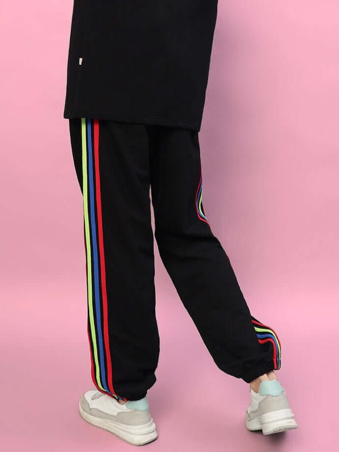 Women's DUDS black joggers with rainbow colorful stripes, tailored fit, shown styled with casual white sneakers.