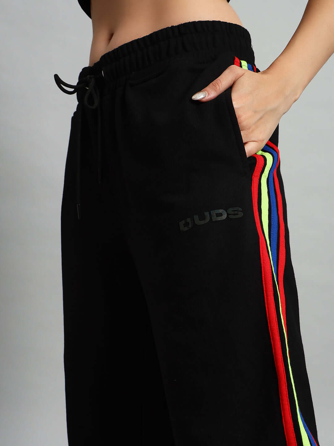 Woman wearing black joggers with colorful rainbow stripes and DUDS logo, hand in pocket, side view, showcasing fit and design.