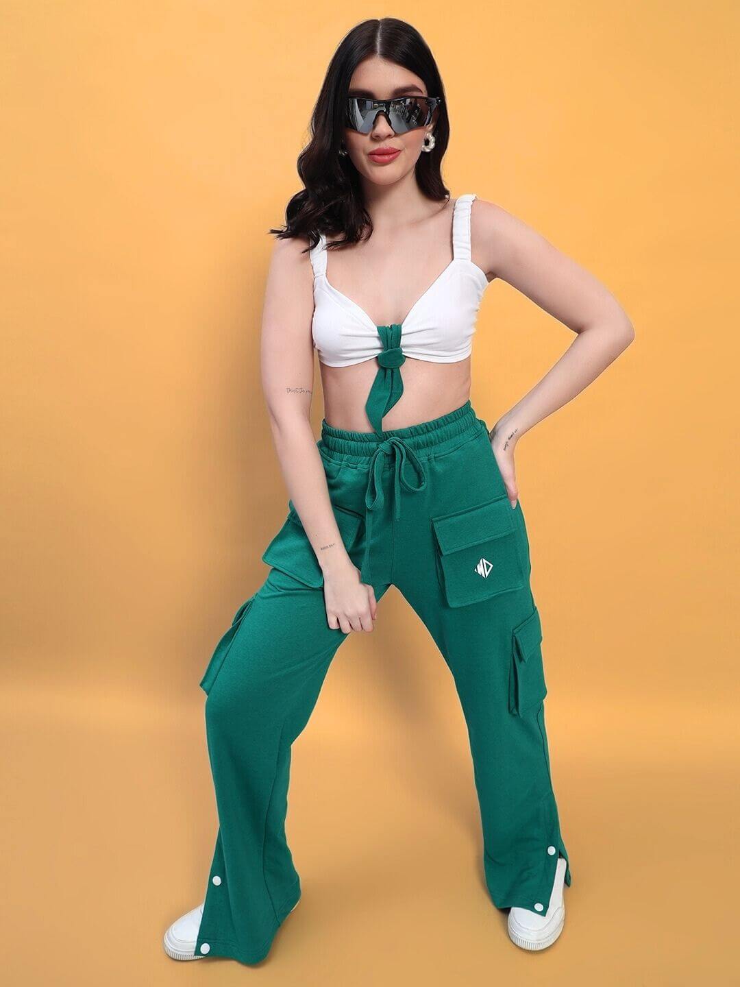 Woman wearing a white Easton crop-top, paired with green pants and sunglasses, posing against an orange background.