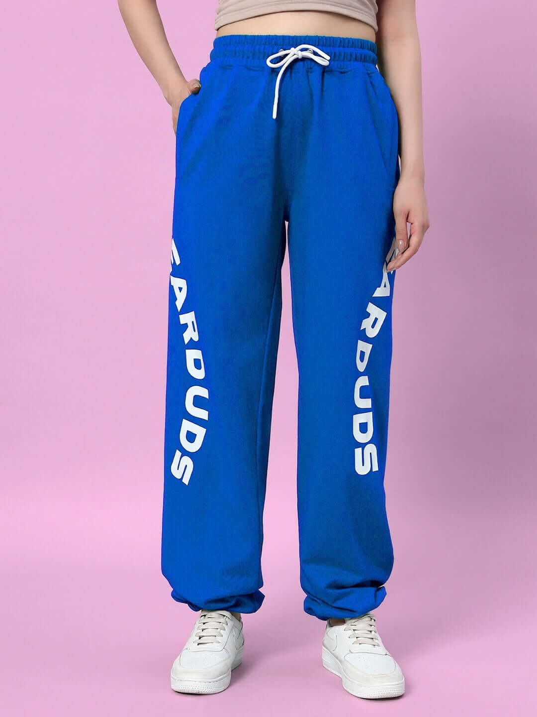 Blue women's relaxed fit jogger pants by DUDS, featuring white logo text along the side, styled with white sneakers.