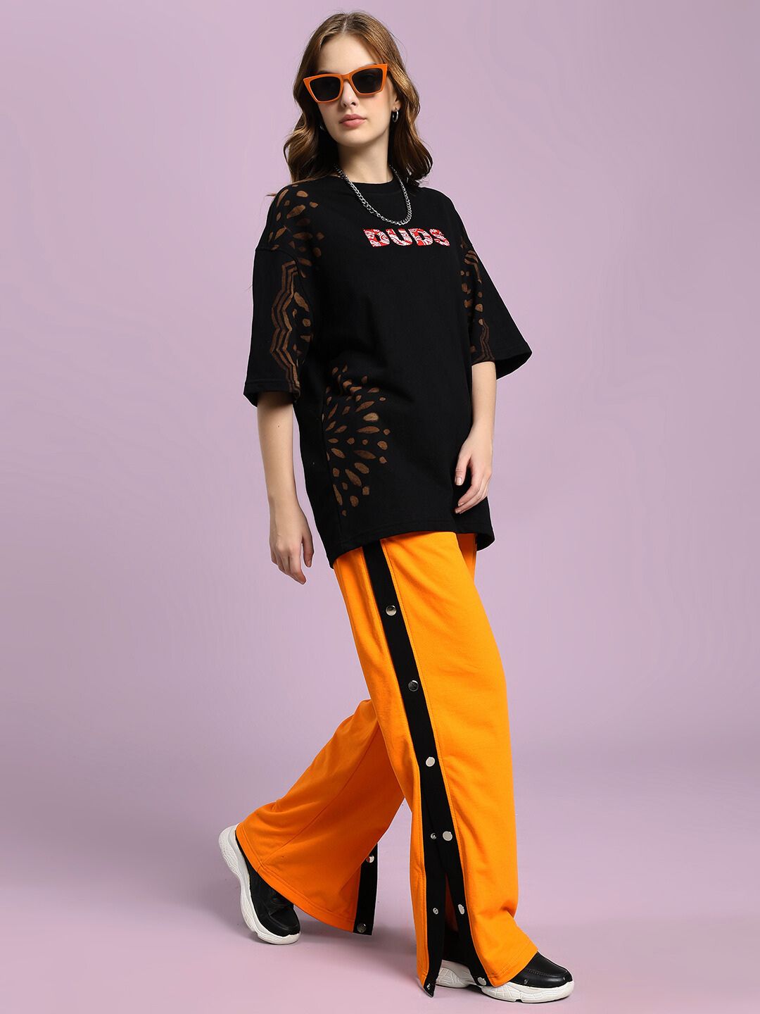 Model wearing WOMEN'S EMBER BOLT SIDE JOGGER ORANGE with sleek side stripes, styled with black sneakers and a casual top, highlighting vibrant fashion.