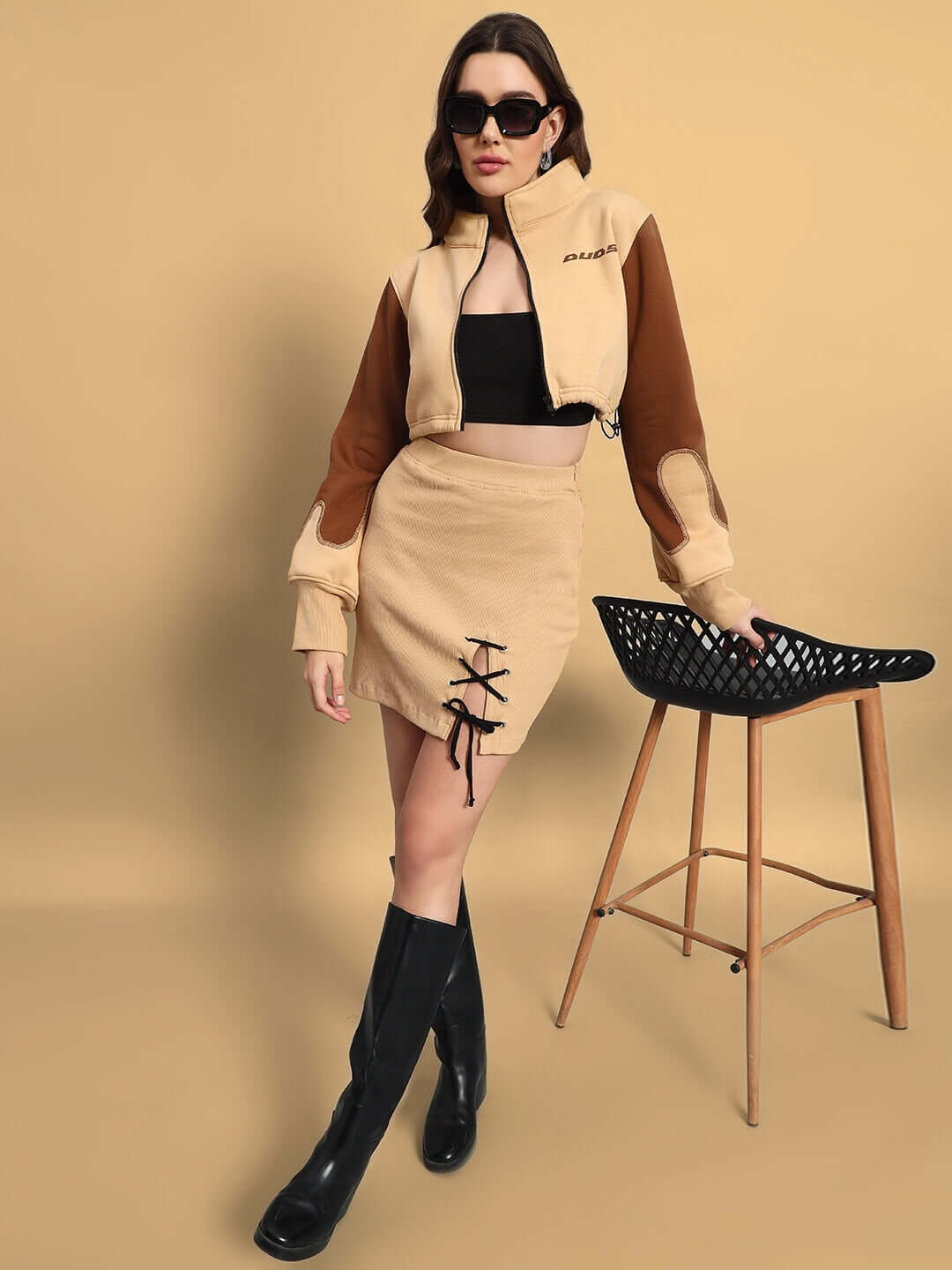 Woman wearing a beige Emma designer skirt with custom fit option, styled with a matching jacket and black boots.