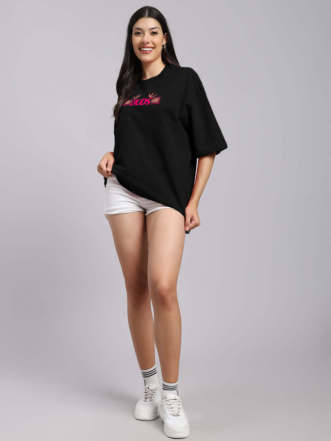 Woman wearing black oversized printed T-shirt made from premium cotton and elastane, paired with white shorts and sneakers.