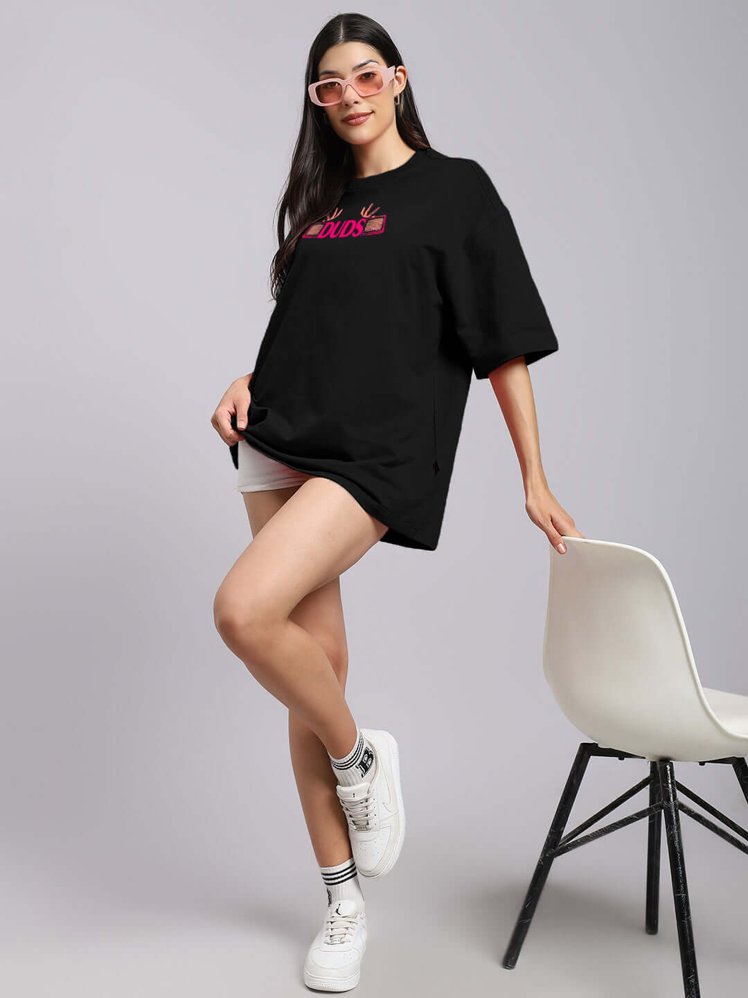 Model wearing women's Eyeconic oversized black printed t-shirt, styled with casual shorts and sneakers.