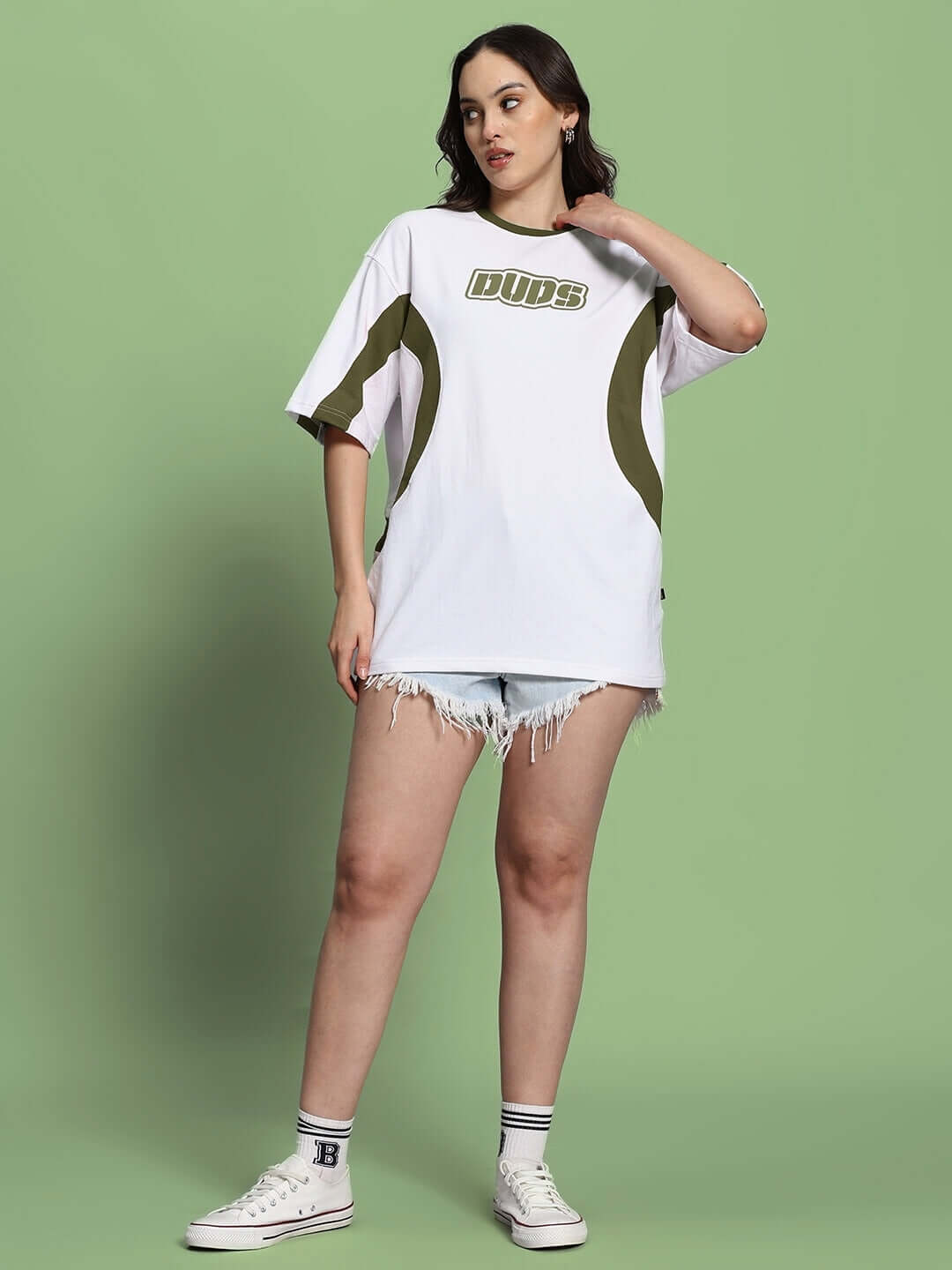 Model wearing oversized women's t-shirt in white and olive green, styled with denim shorts, showcasing casual fashion.