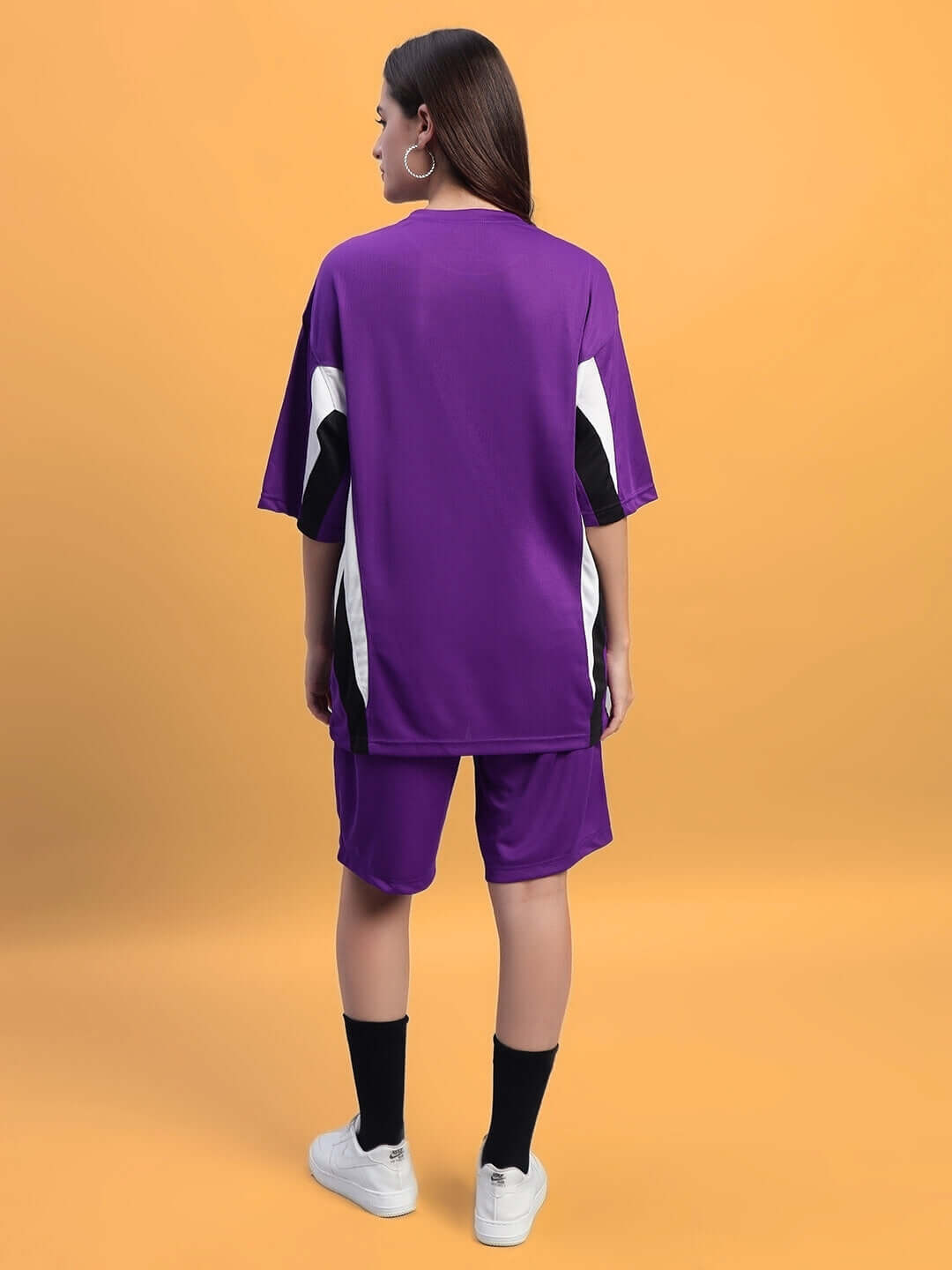 Rear view of a woman wearing a purple Women's FIFA Colorblock Co-Ord Set against a yellow background.