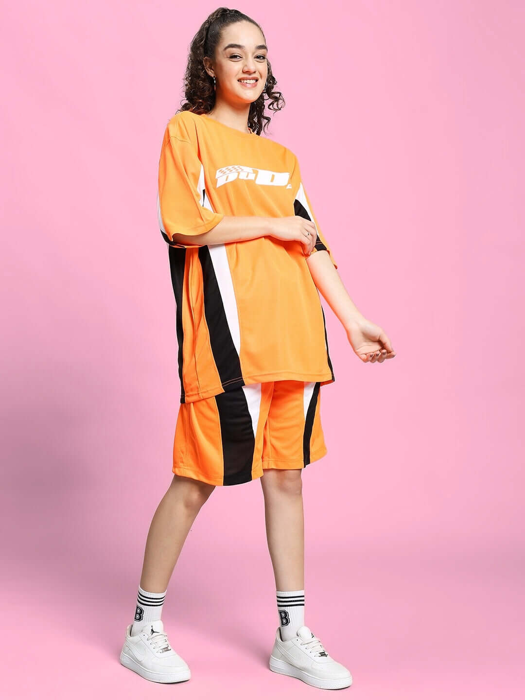 Woman wearing WOMEN'S FIFA COLORBLOCK CO-ORD SET ORANGE against pink background, showcasing sporty and elegant activewear fashion.