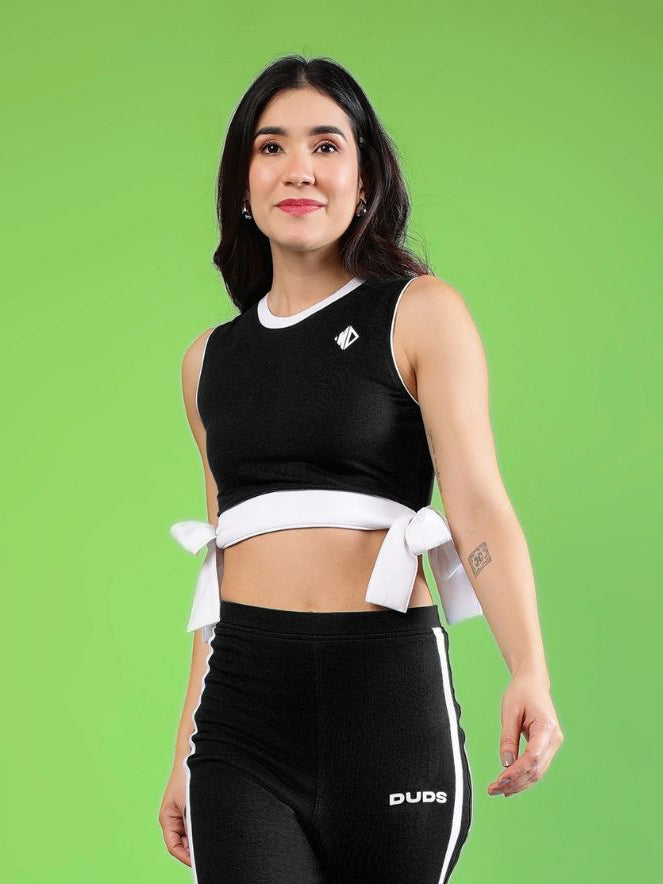 WOMENS FITTONIA COOL CROP TOP BLACK worn by a woman in front of a green background, showcasing its stylish design.
