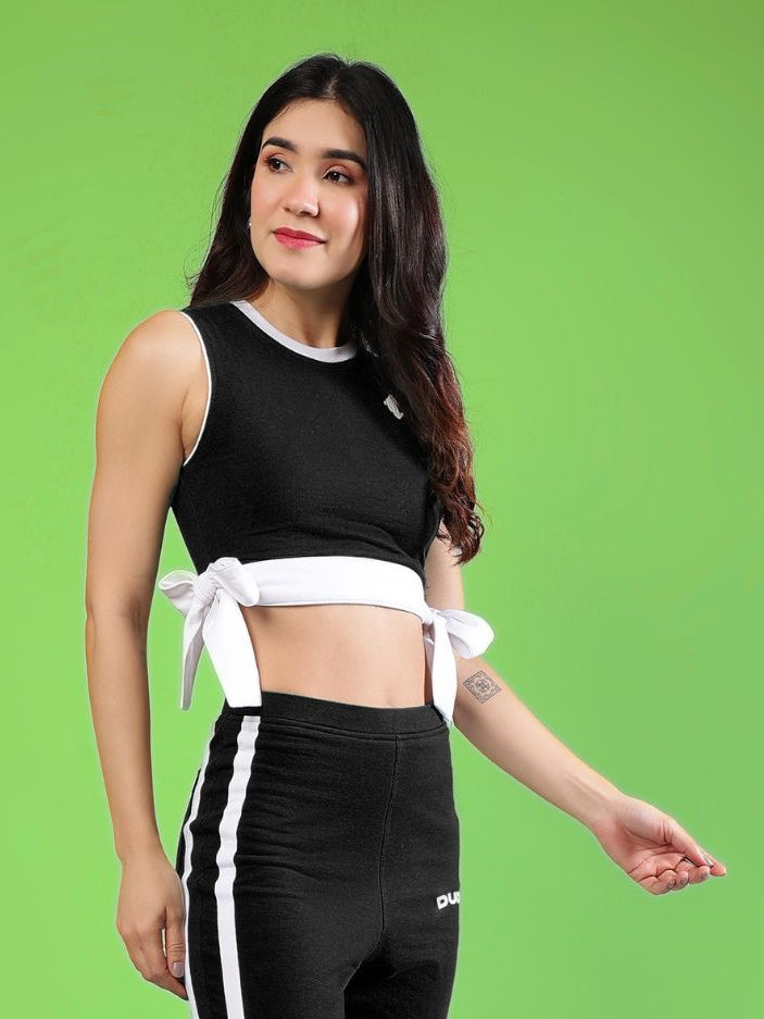 WOMENS FITTONIA COOL CROP TOP BLACK on a model against a green background, showcasing its stylish design and comfortable fit.
