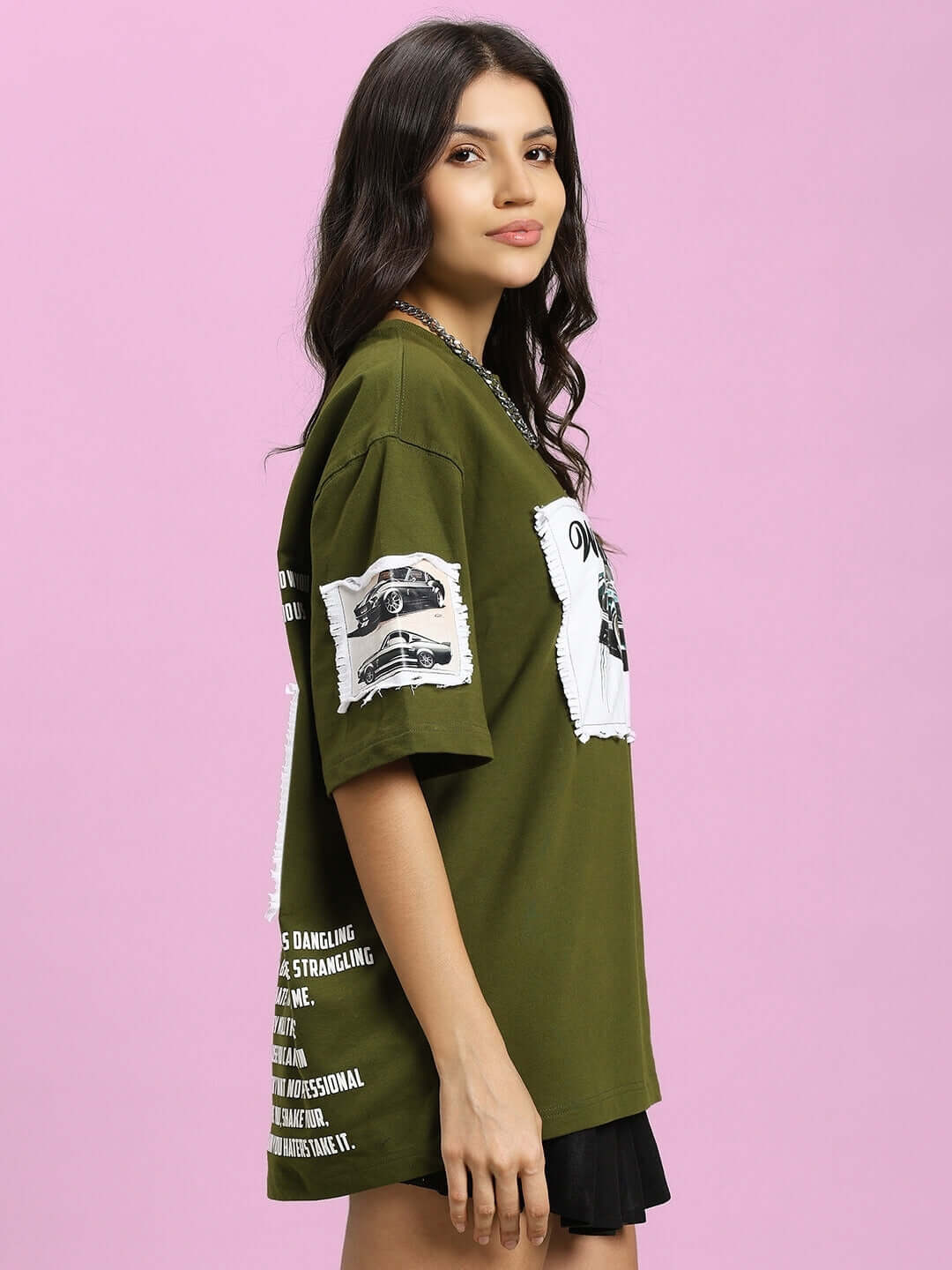 Woman wearing an olive green oversized t-shirt with Ford Mustang design, side view against a pink background.