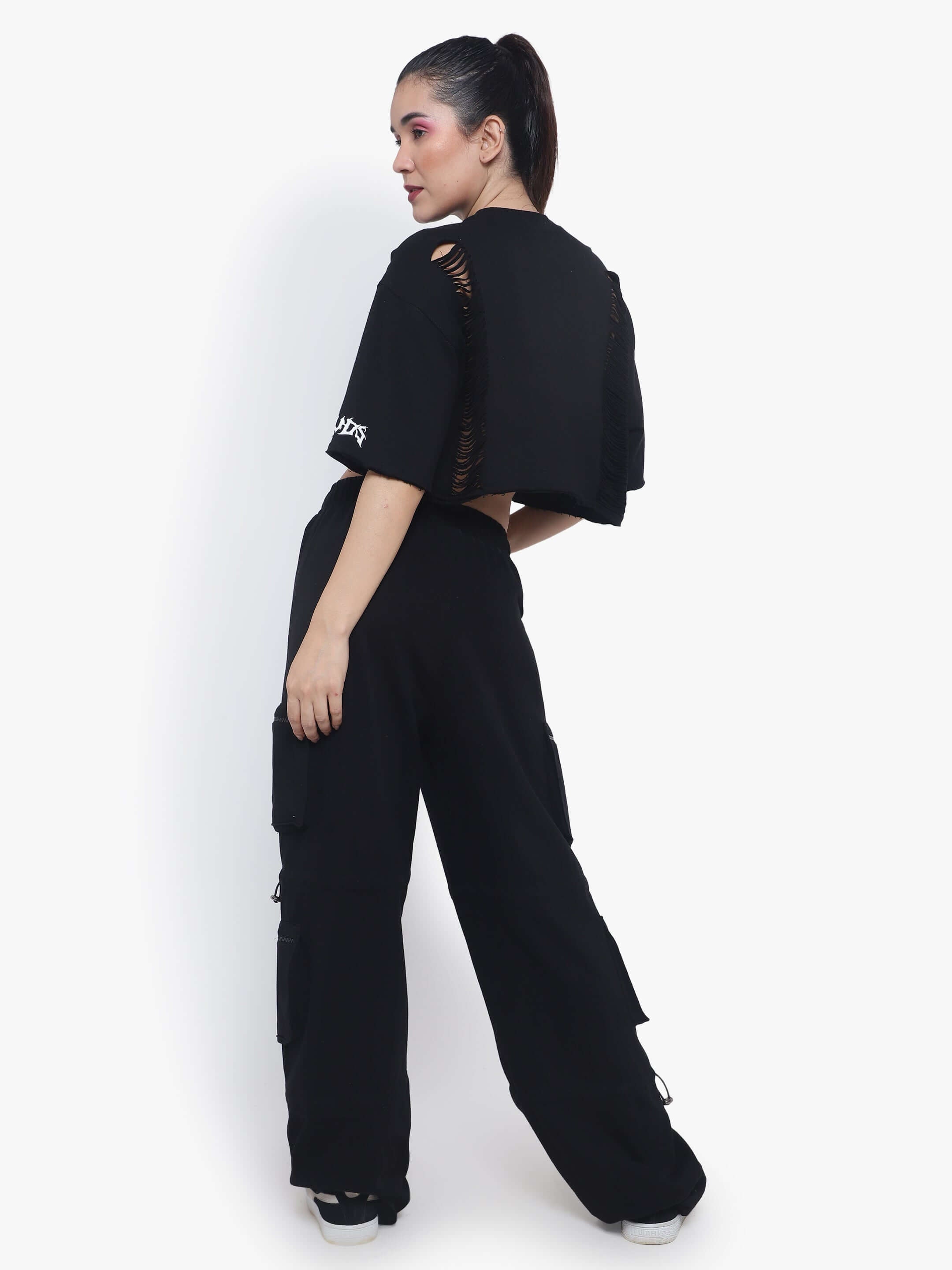 Woman wearing black oversized cropped t-shirt with ripped design, styled with high-waisted black pants. Fashionable casual look.