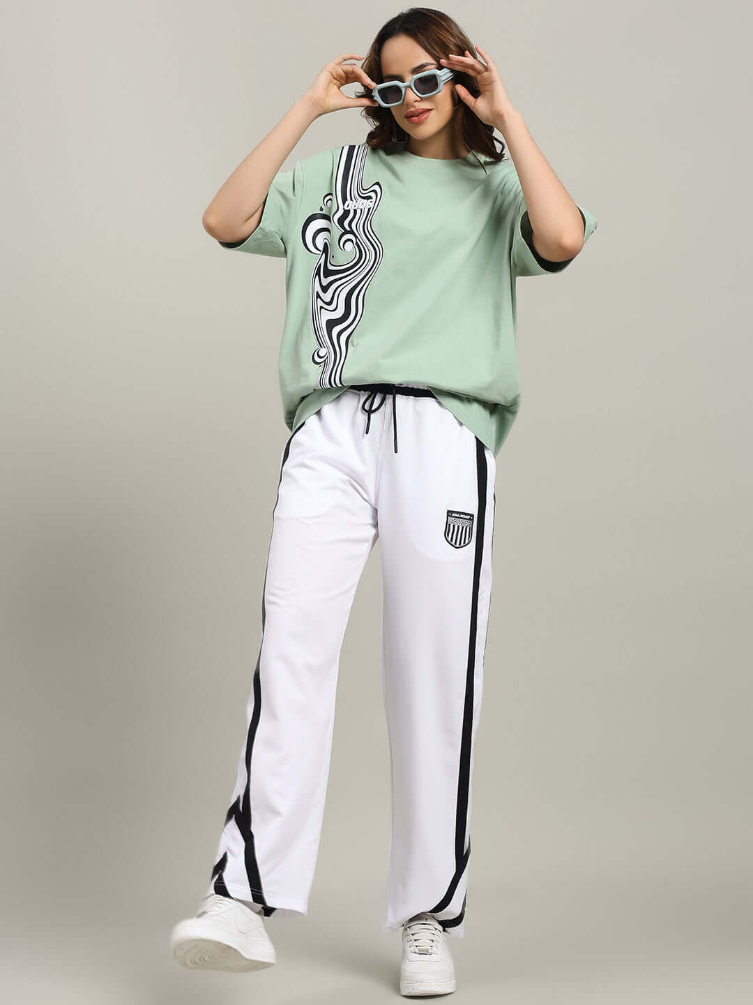 Model wearing WOMEN'S FRIZZLE RELAXED FIT JOGGER WHITE with a green top and sunglasses; comfortable, stylish joggers made by DUDS.