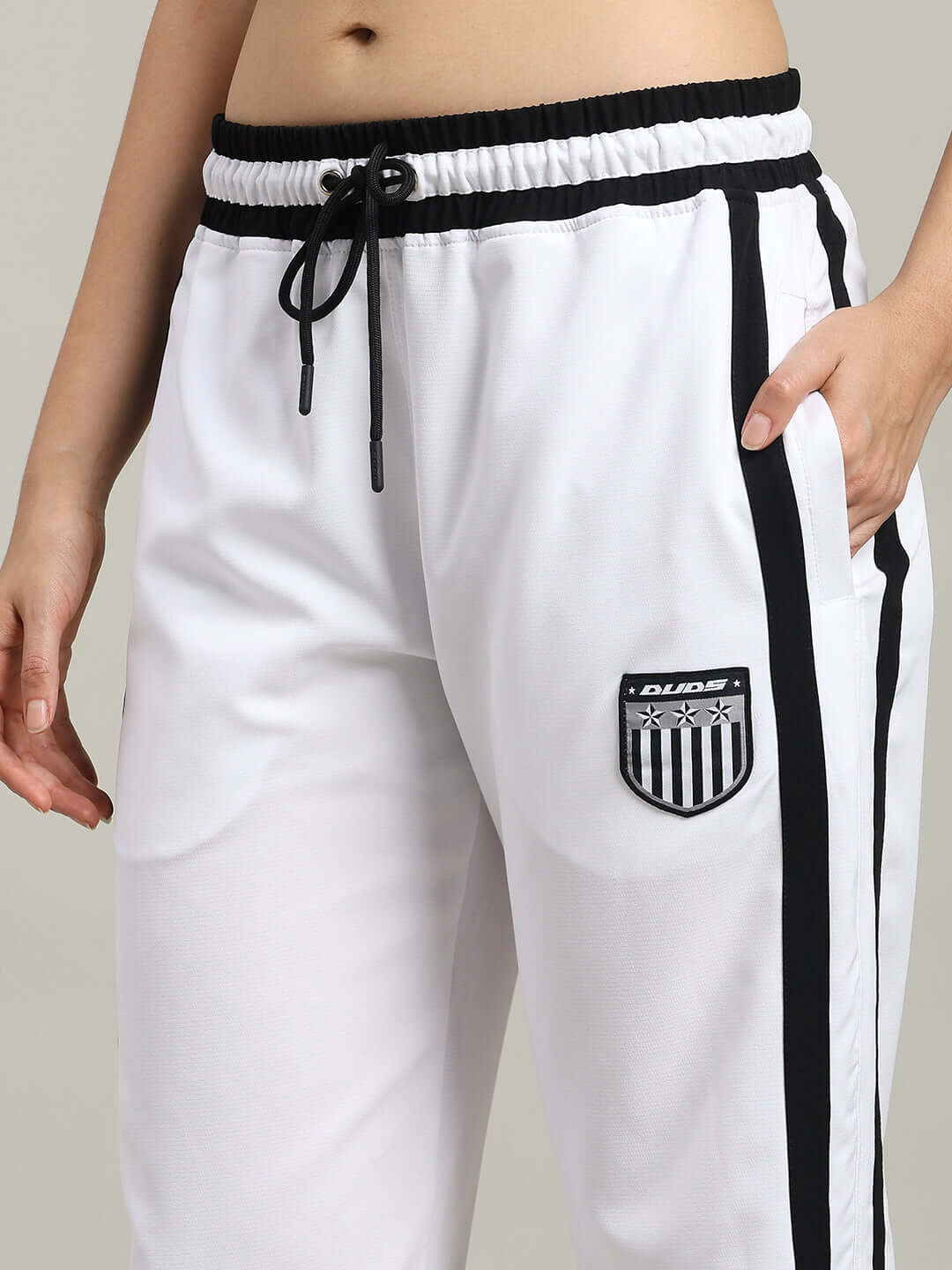 Close-up of WOMEN'S FRIZZLE RELAXED FIT JOGGER WHITE with black stripe details and DUDS logo patch.