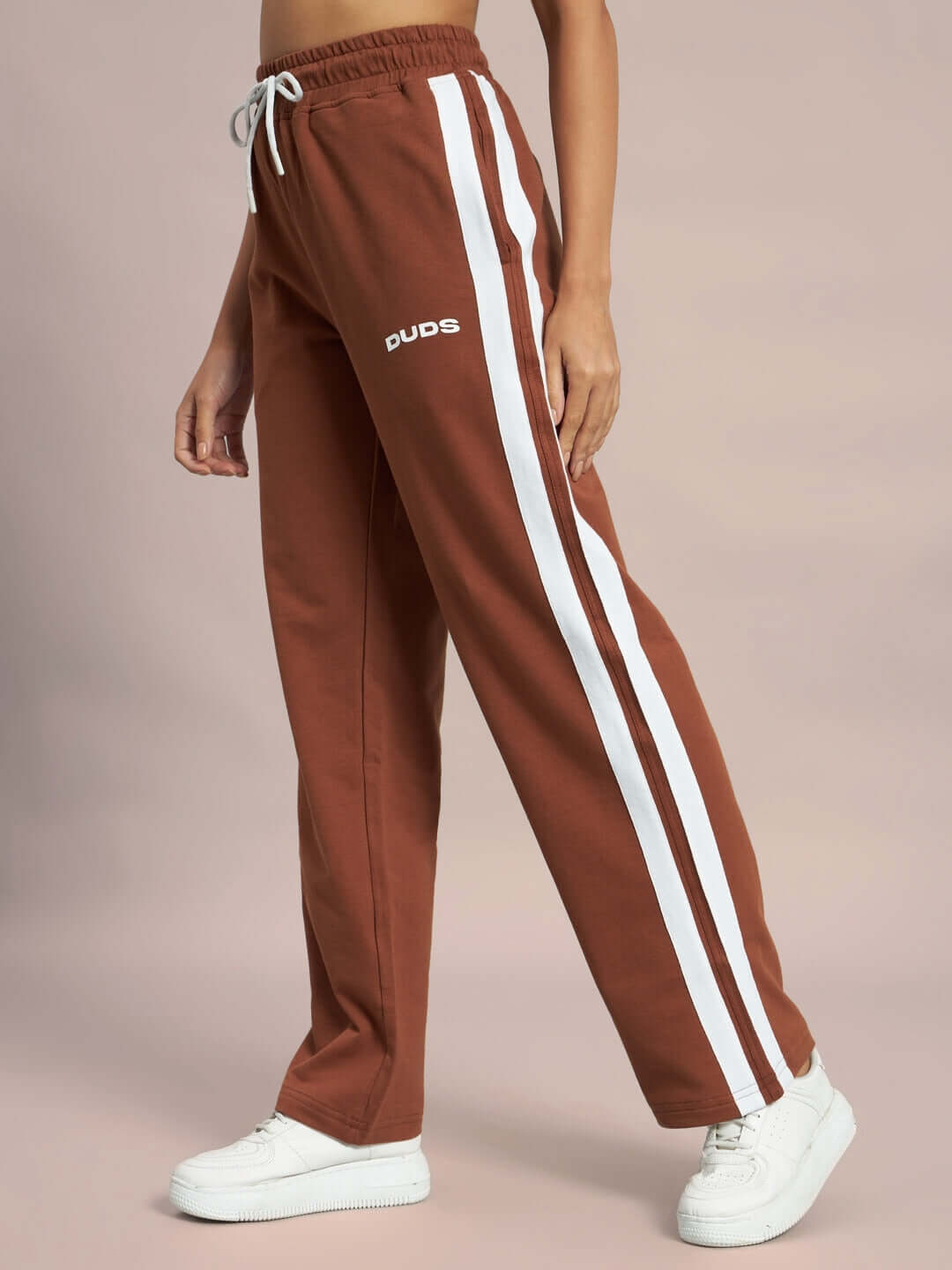 Woman wearing brown Future Icon 2 Stripe Jogger with white stripes and sneakers, made by DUDS, customizable fit option available.