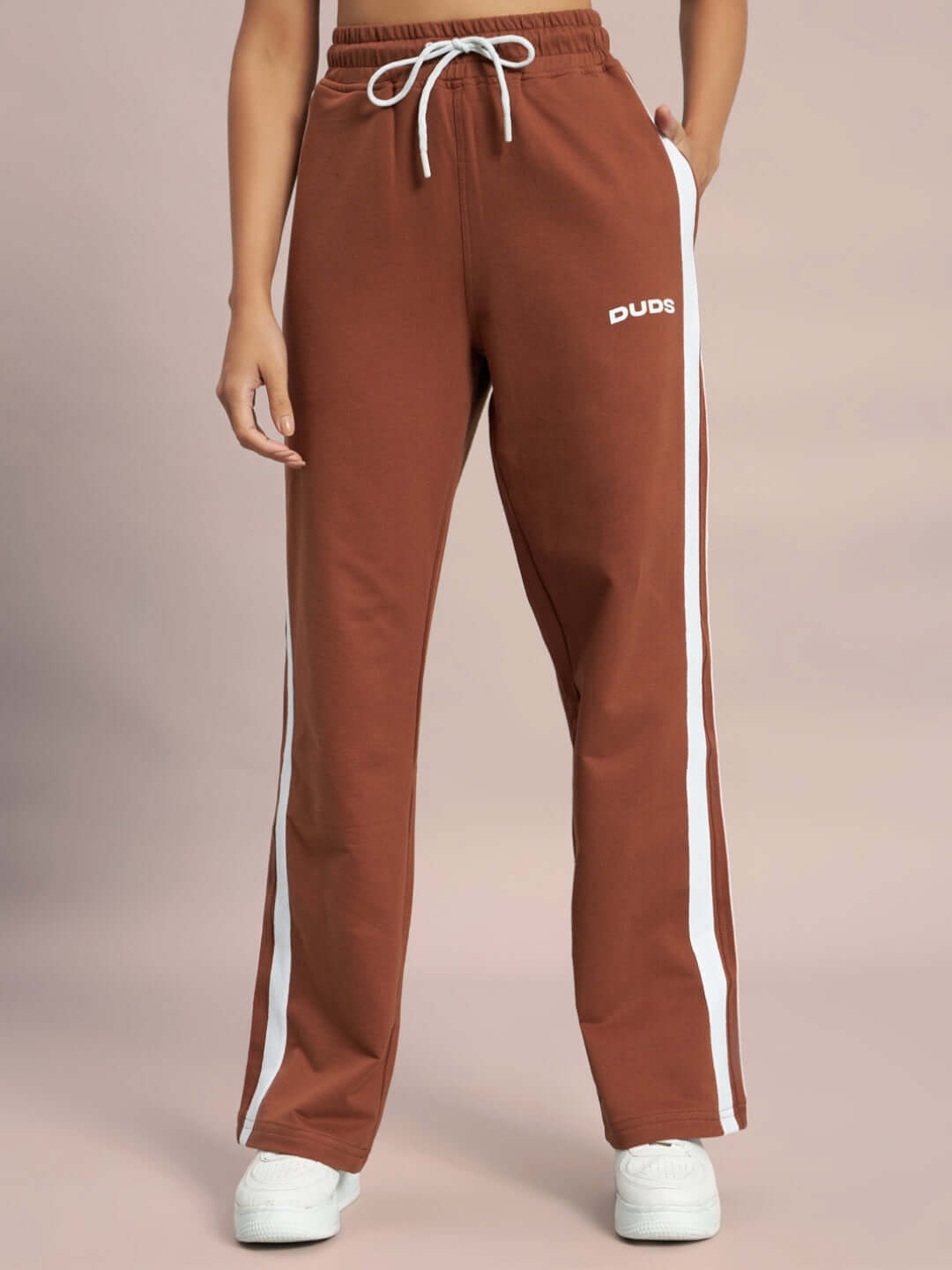 Brown jogger pants with white stripes and DUDS logo, worn by a woman. Stylish, made-to-order sweatpants available in custom fit.