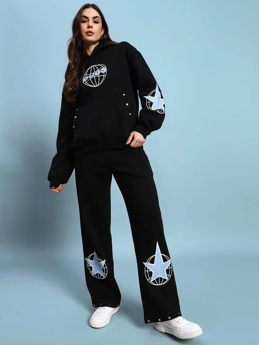 Woman modeling WOMEN GLOBAL FLEECE HOODIE BLACK with star designs against a blue background.