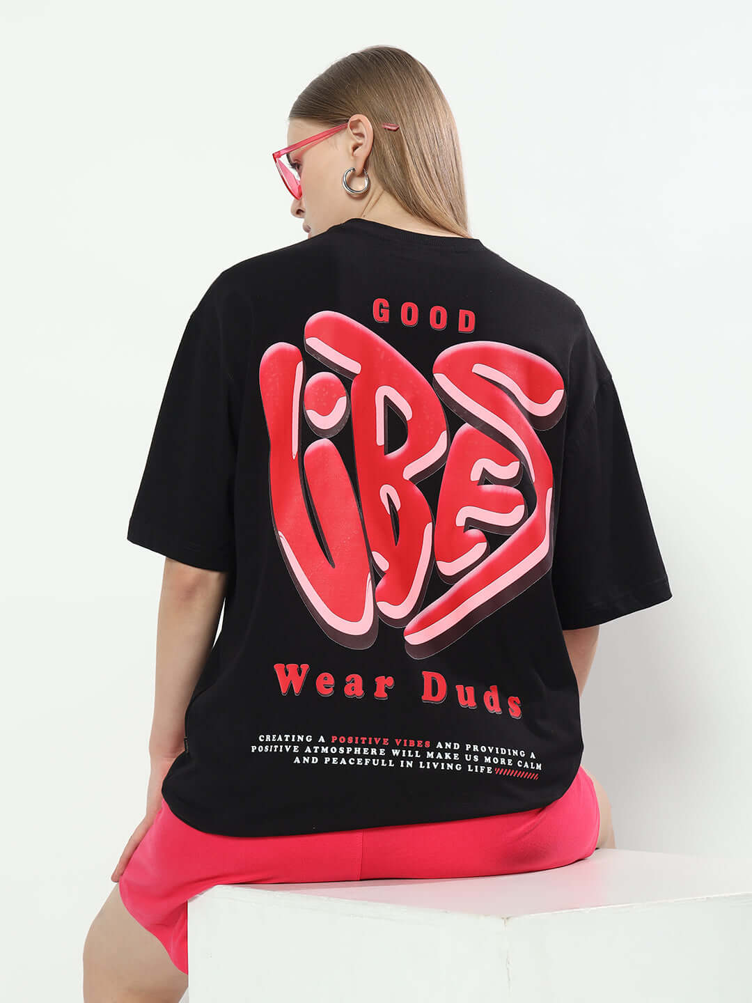 Woman wearing an oversized black t-shirt with 'Good Vibes' print, promoting DUDS brand. Ideal for customizable fashion lovers.