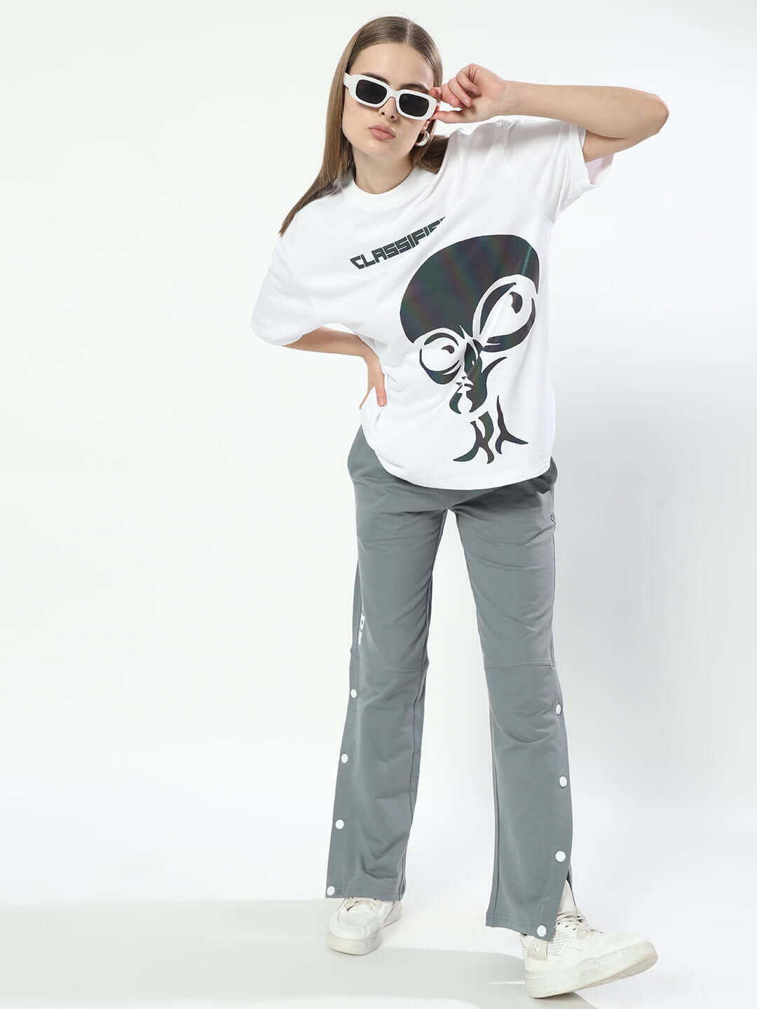 Woman wearing grey racer joggers paired with a casual white graphic tee and sneakers, striking a stylish pose against a white background.