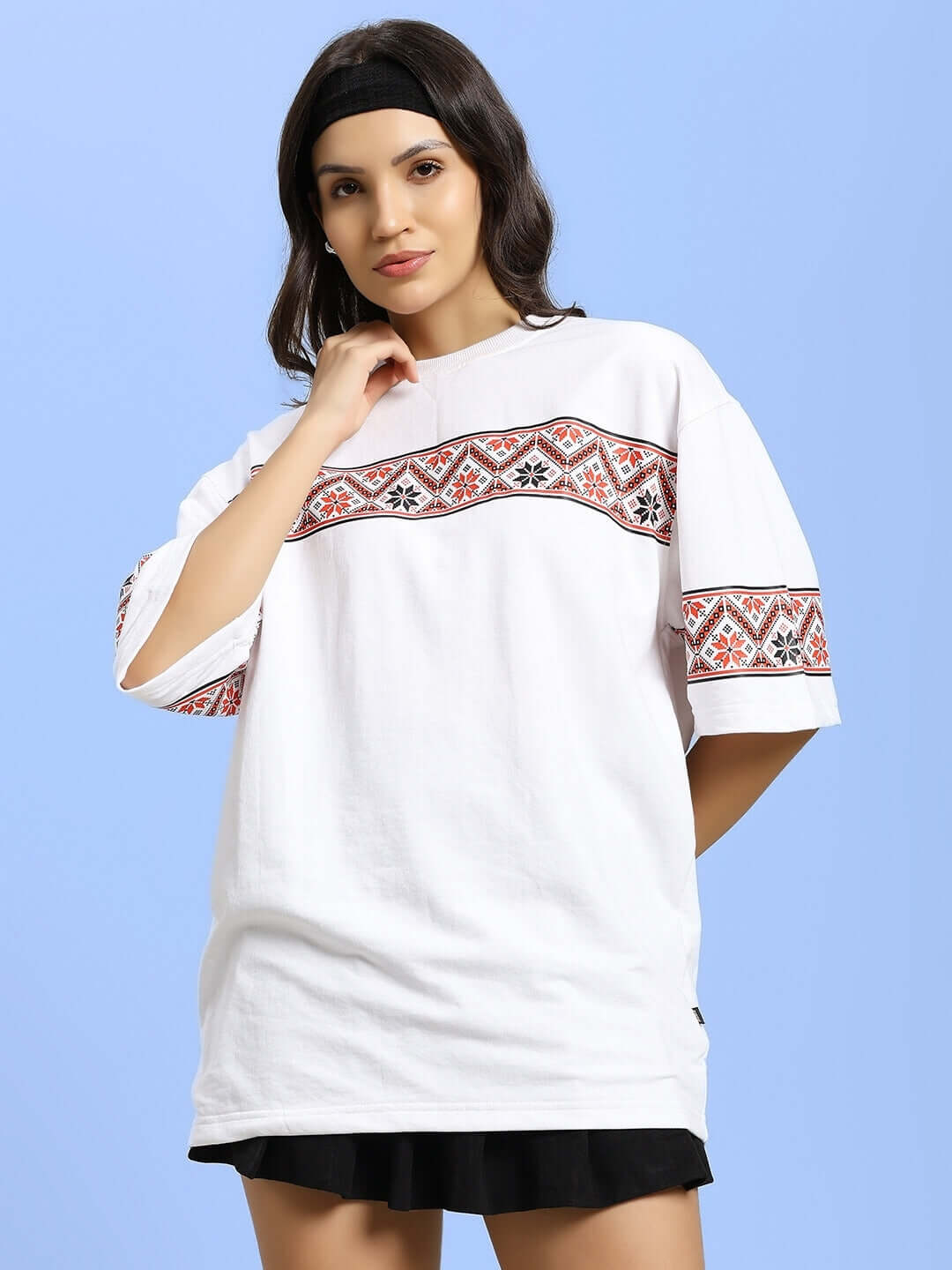 Woman wearing white T-shirt with Vyshyvanka print, made of premium cotton-blend fabric, styled elegantly against a light blue background.
