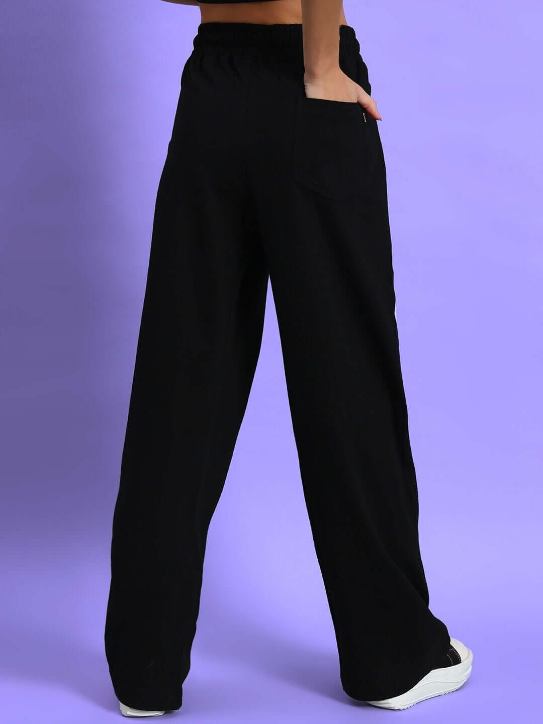 Woman wearing black relaxed-fit joggers from DUDS, highlighting comfortable high-speed fashion and custom fit option on a purple background.